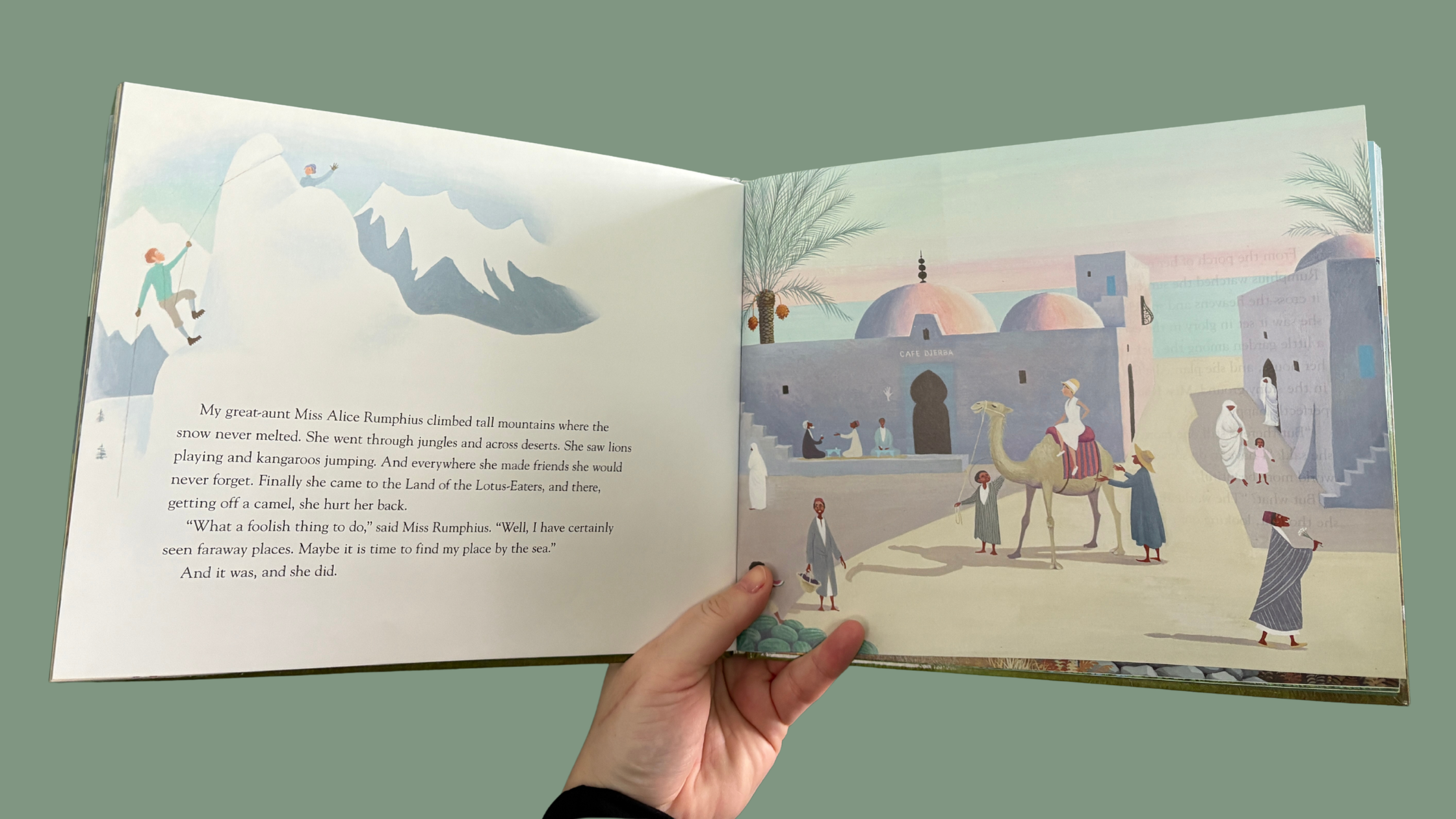Miss Rumphius children's book open to the page showing her travels — mountain climbing illustration on the left, desert marketplace scene with camels on the right, held against a sage green background