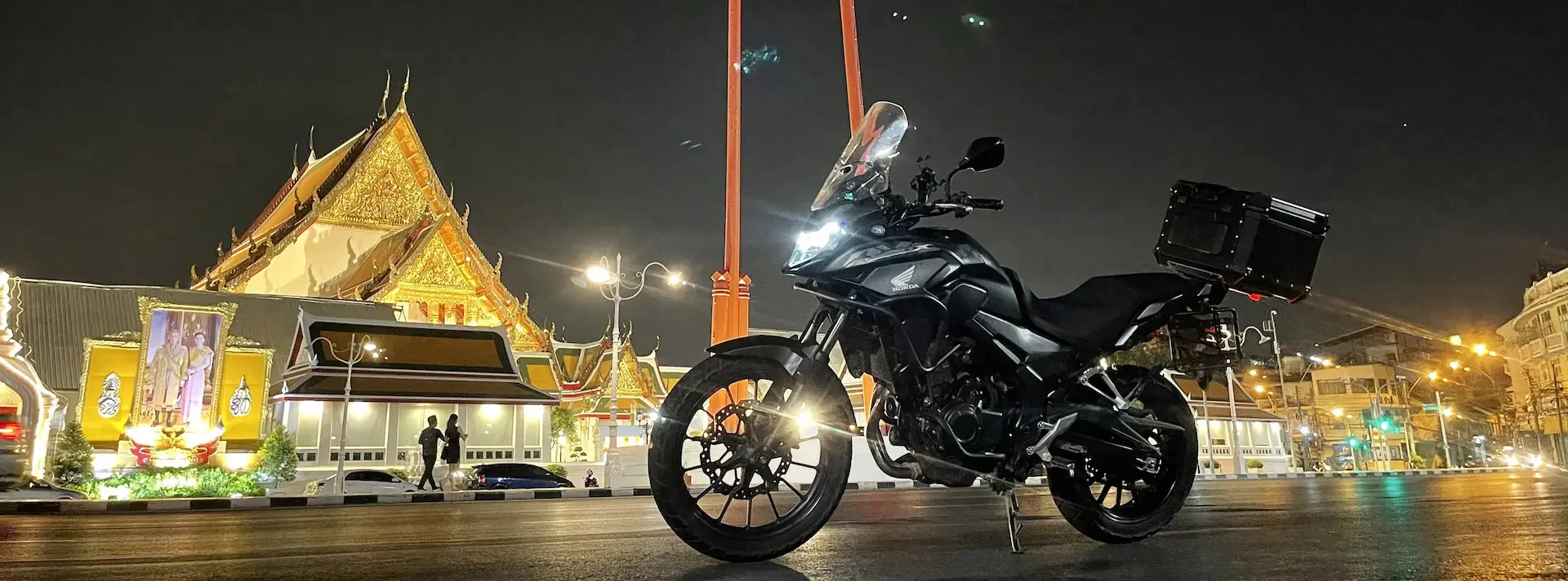 A black Honda motorcycle parked on a street at night with a brightly lit temple in the background.