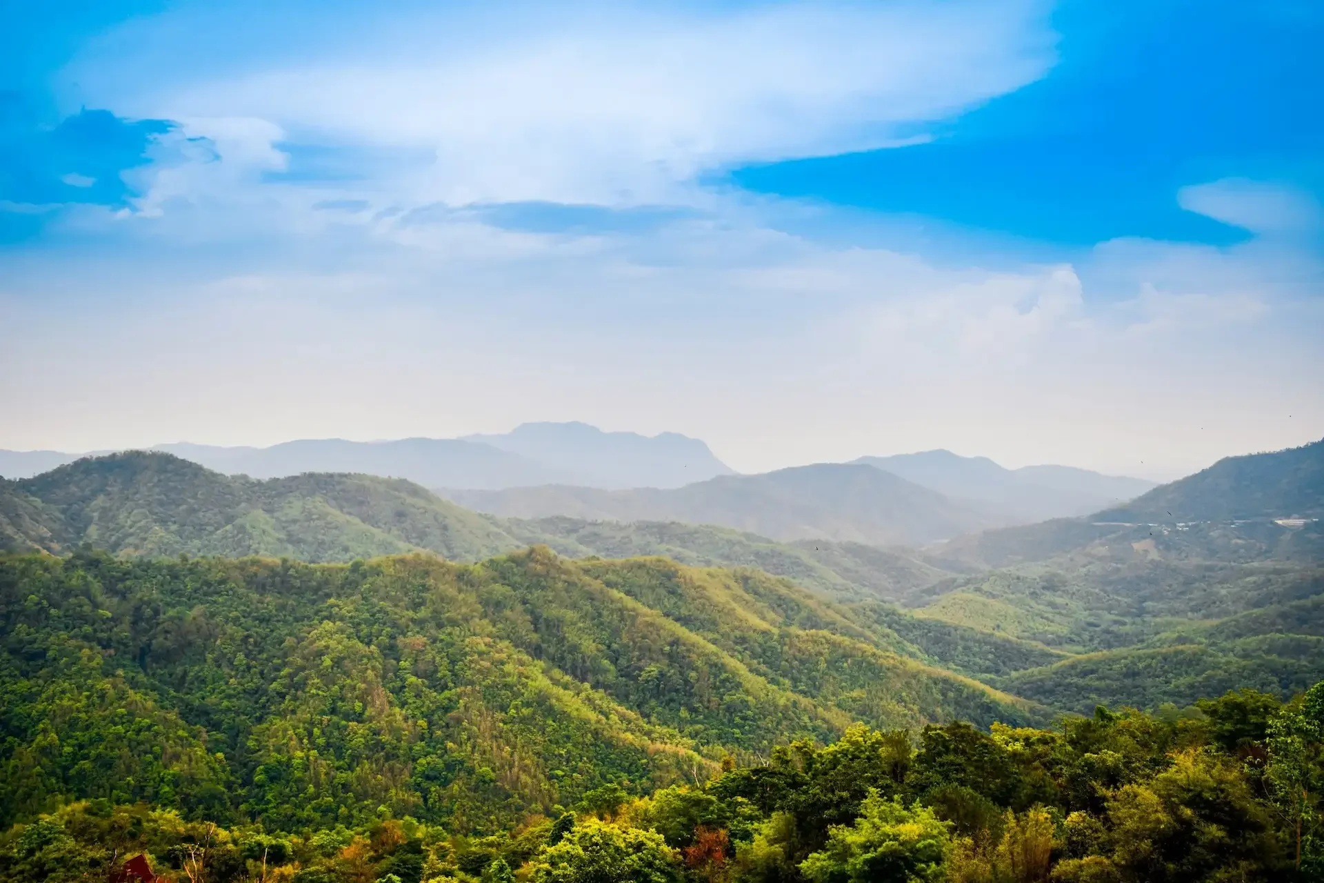 Panoramic view of green hills and mountains with a partly cloudy sky.
