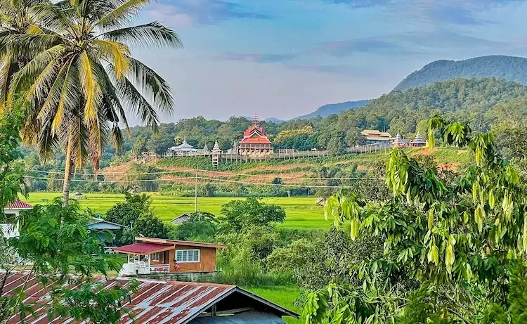 Lush green landscape with trees, hills, and a village with traditional buildings along the Mae Hong Son Loop in northern Thailand