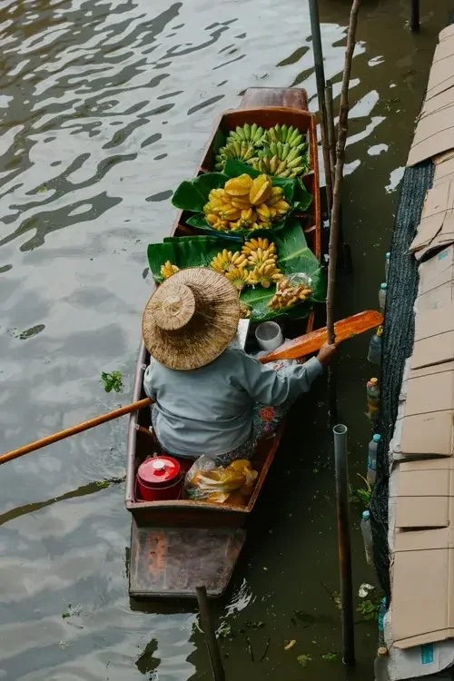 A person wearing a traditional Thai clothing in a small boat selling food at the floating market in Thailand