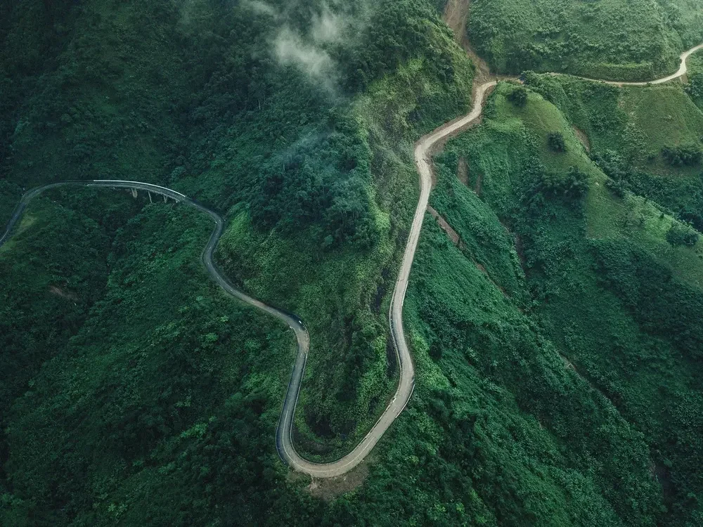 A winding mountain road surrounded by lush green forest and vegetation.