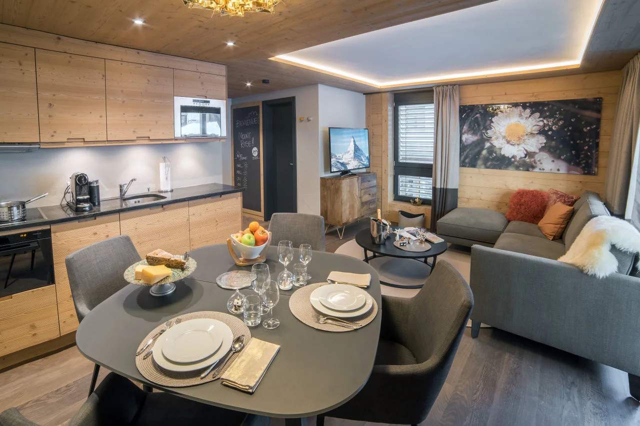A lift or stairs take you to the apartment’s open plan living and dining area with a balcony. Here you can relax on the ‘L’ shaped sofa in front of the TV and enjoy meals around the dining table, prepared in the kitchenette. Perfect for a couple or two friends looking for a convenient base in central Zermatt, the apartment has one double/twin bedroom with a bathroom. There is a guest WC in the hallway. The shared facilities of the residence include a ski room with private ski lockers and a laundry room with all the necessary utilities. BOOK NOW