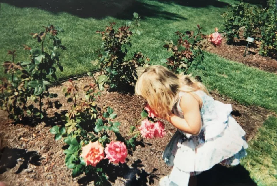 Young Brittany Corrales smelling pink roses in a rose garden
