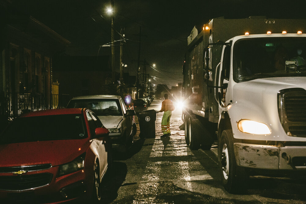  New Orleans, LA - March 24, 2020 - Bryan Bowman empties residential garbage cans into the back of a Metro Service Group truck in the 7th Ward of New Orleans. His employer has begun furnishing extra rubber gloves, facemasks, and handkerchiefs to thei