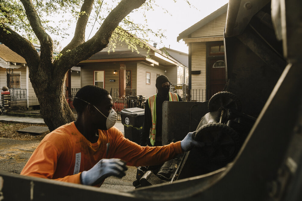 New Orleans, LA - March 24, 2020 - Bryan Bowman (L) and Landrius Cooley empty residential garbage cans into the back of a Metro Service Group truck in the 7th Ward of New Orleans. His employer has begun furnishing extra rubber gloves, facemasks, and