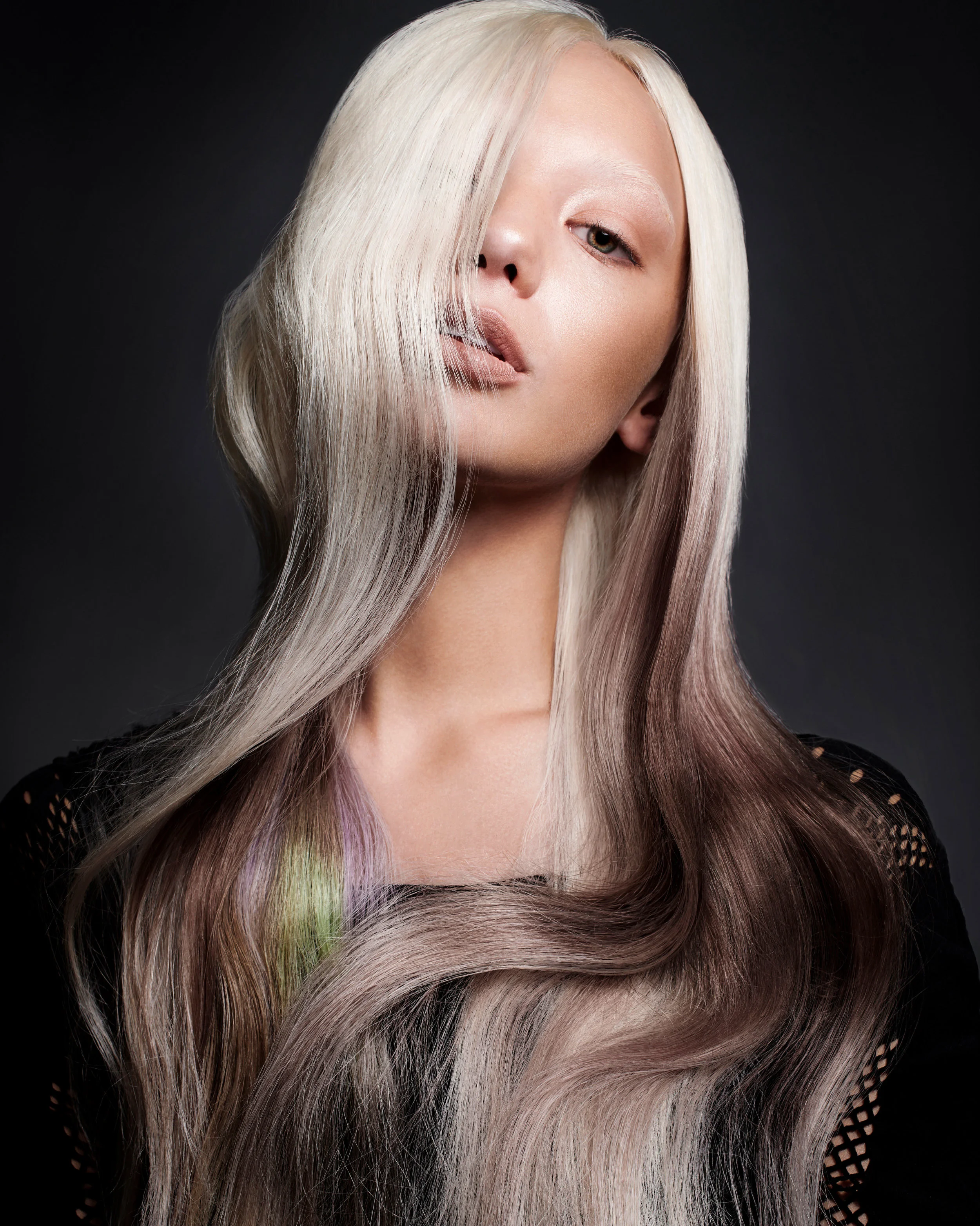 A woman with platinum blonde hair styled in loose waves against a dark background.