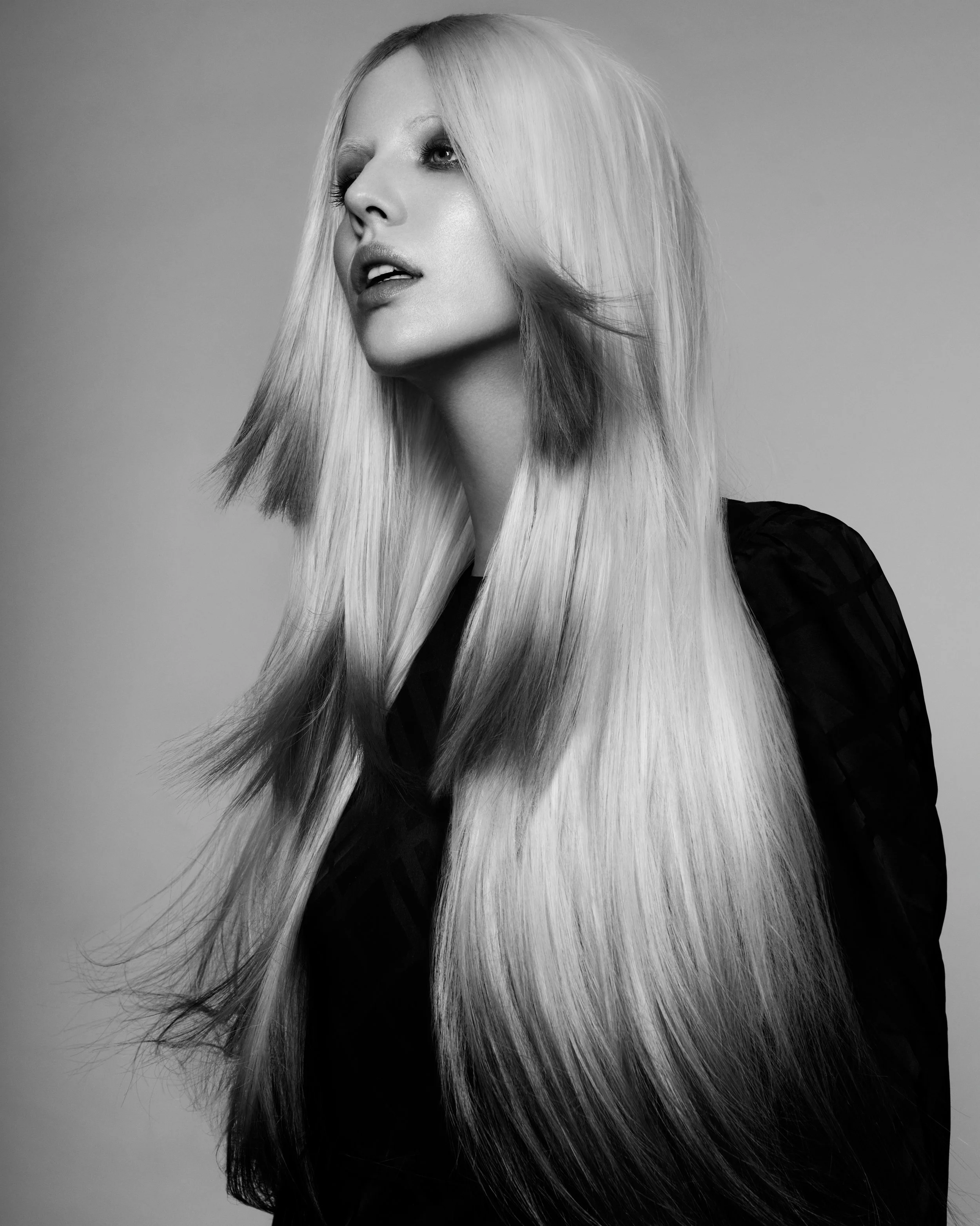 Black and white portrait of a woman with long, straight blonde hair, looking to her left with a neutral expression.
