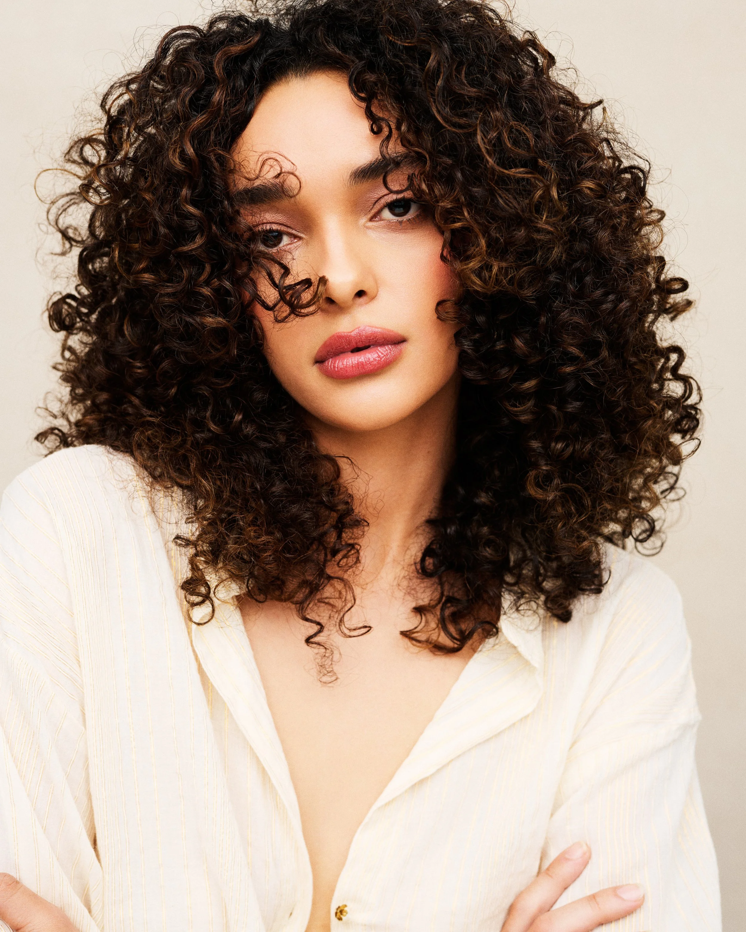 Close-up of a woman with curly dark hair, wearing a cream-colored shirt with a plunging neckline.