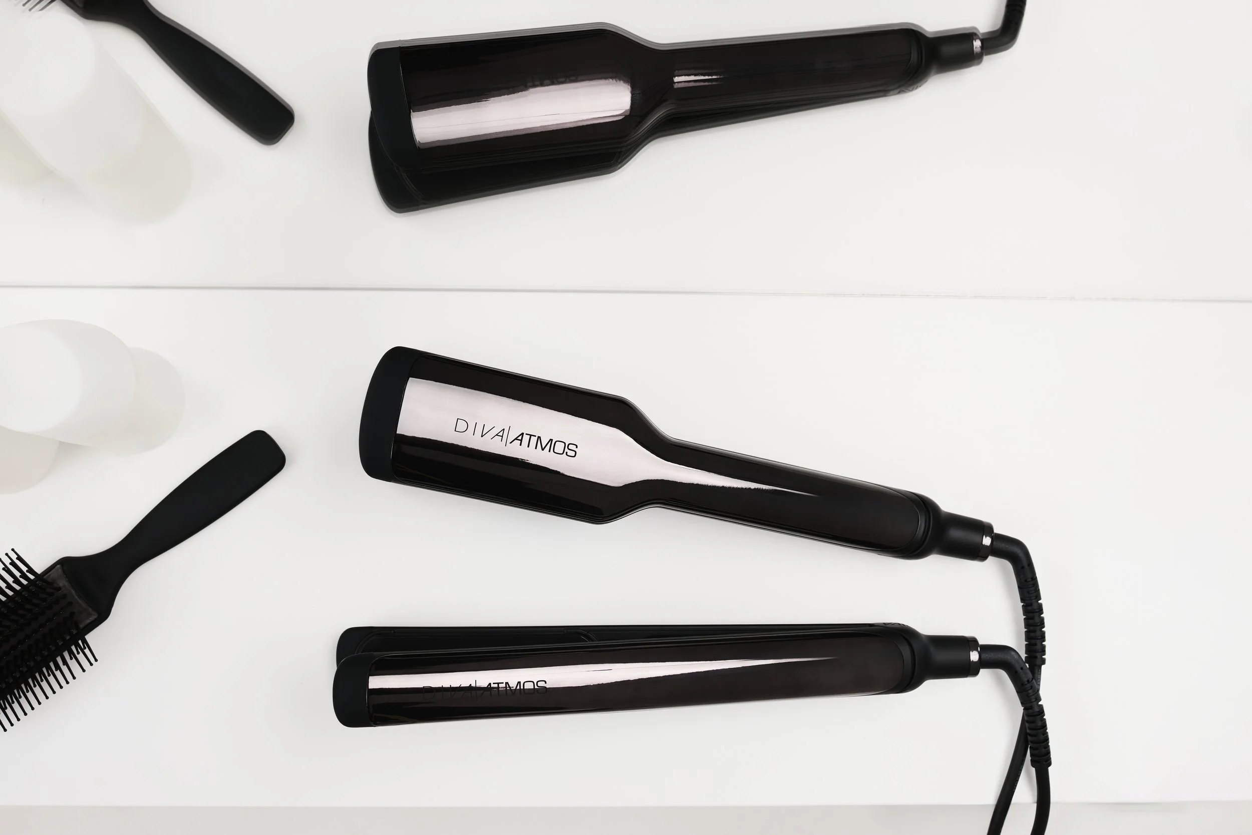 Assorted hair styling tools on a white surface, including a hairdryer, a curling iron, a hairbrush, and a bottle of conditioner.