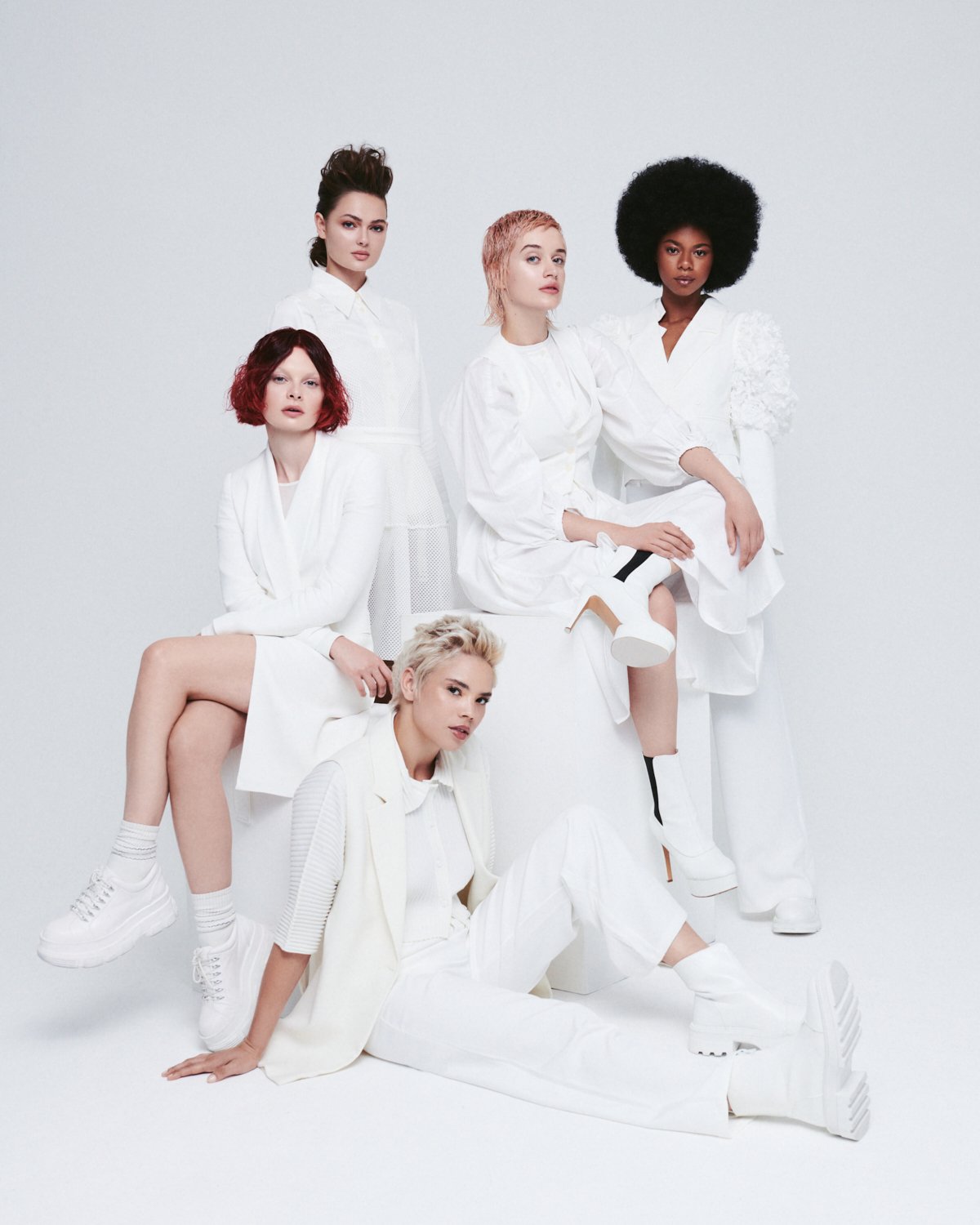 Group of six women with diverse hairstyles and skin tones dressed in white, posing against a plain white background.