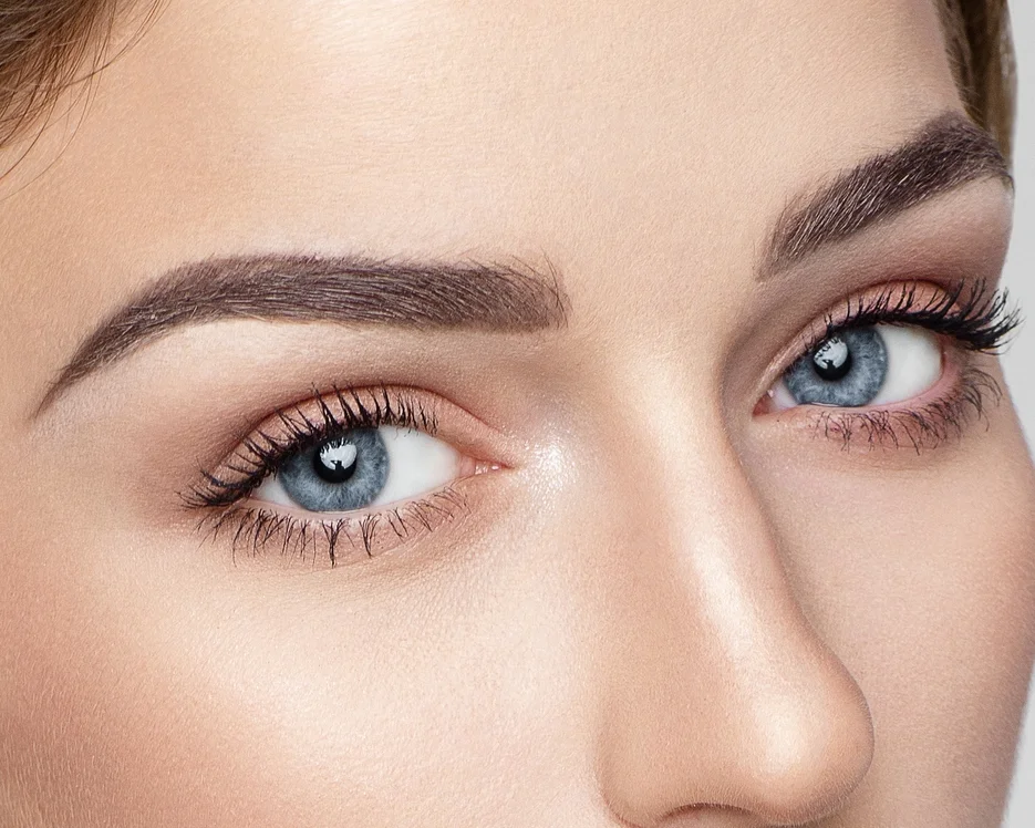 Close-up of a woman's face focusing on her blue eyes, well-groomed eyebrows, long eyelashes, and smooth skin.