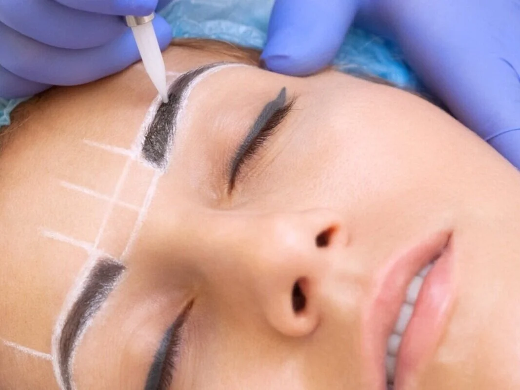 A woman receiving a microblading procedure on her eyebrows from a technician wearing purple gloves.