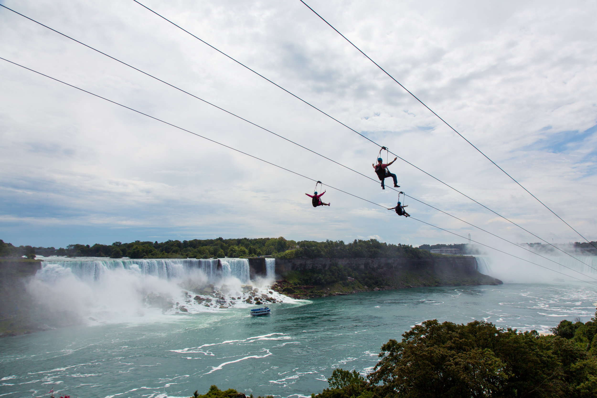 Zip liners take a ride on the Canadian side, with the American falls, and the Maid of the Mist in the background.