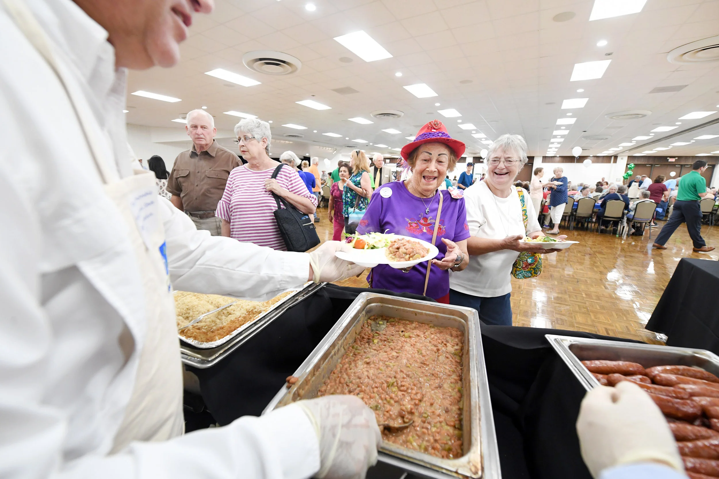 Lenora Patranella, center, and Micki Miskimen make their way through the food line at the Brazos Center on Wednesday, Aug. 8, 2018, during the annual Feast of Caring, a fundraiser for the Brazos Valley Food Bank. Plates of rice, beans, sausage, salad, bread and dessert were served during the lunchtime event, which also raised awareness of food insecurity in the Brazos Valley. (Laura McKenzie/The Eagle)