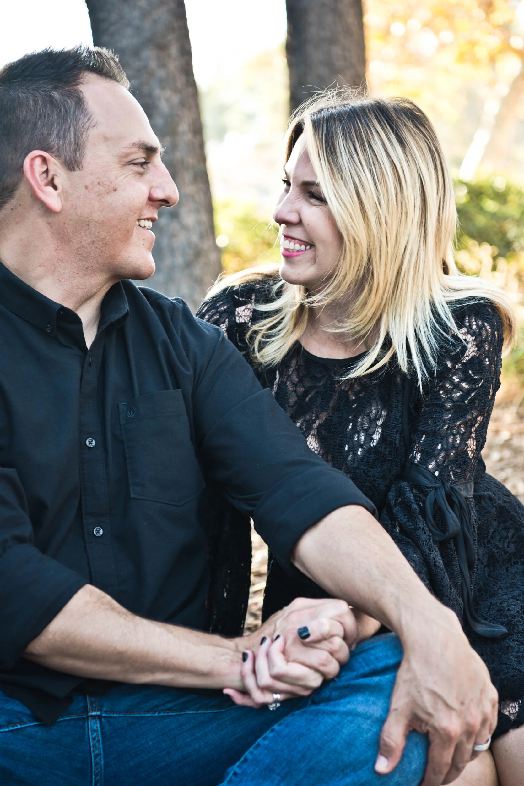 Dad and mom sitting in a grove of cedar trees holding hands and smiling at each other.