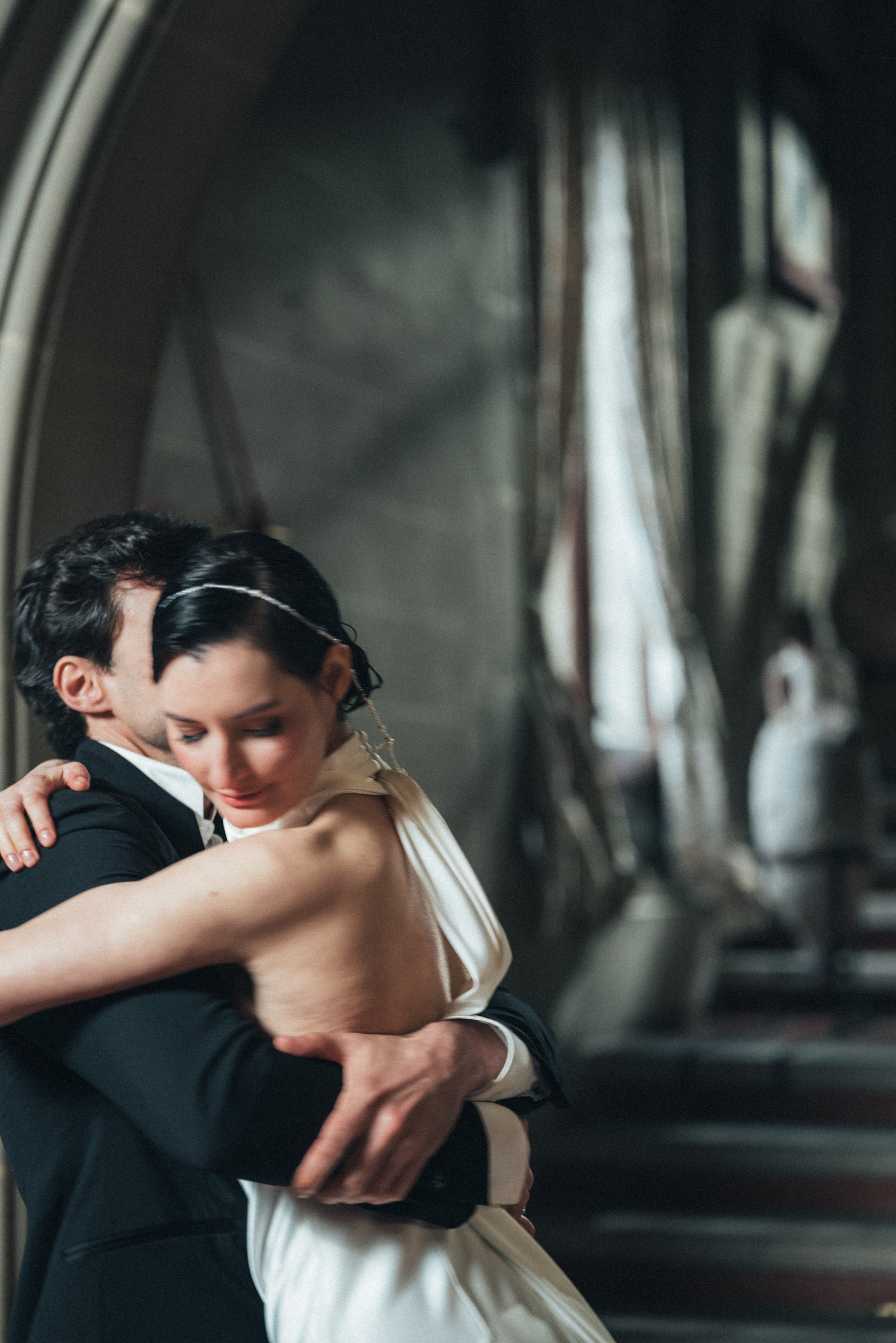 Bride and groom hugging in a dimly lit setting, bride in a white dress, groom in a black suit.
