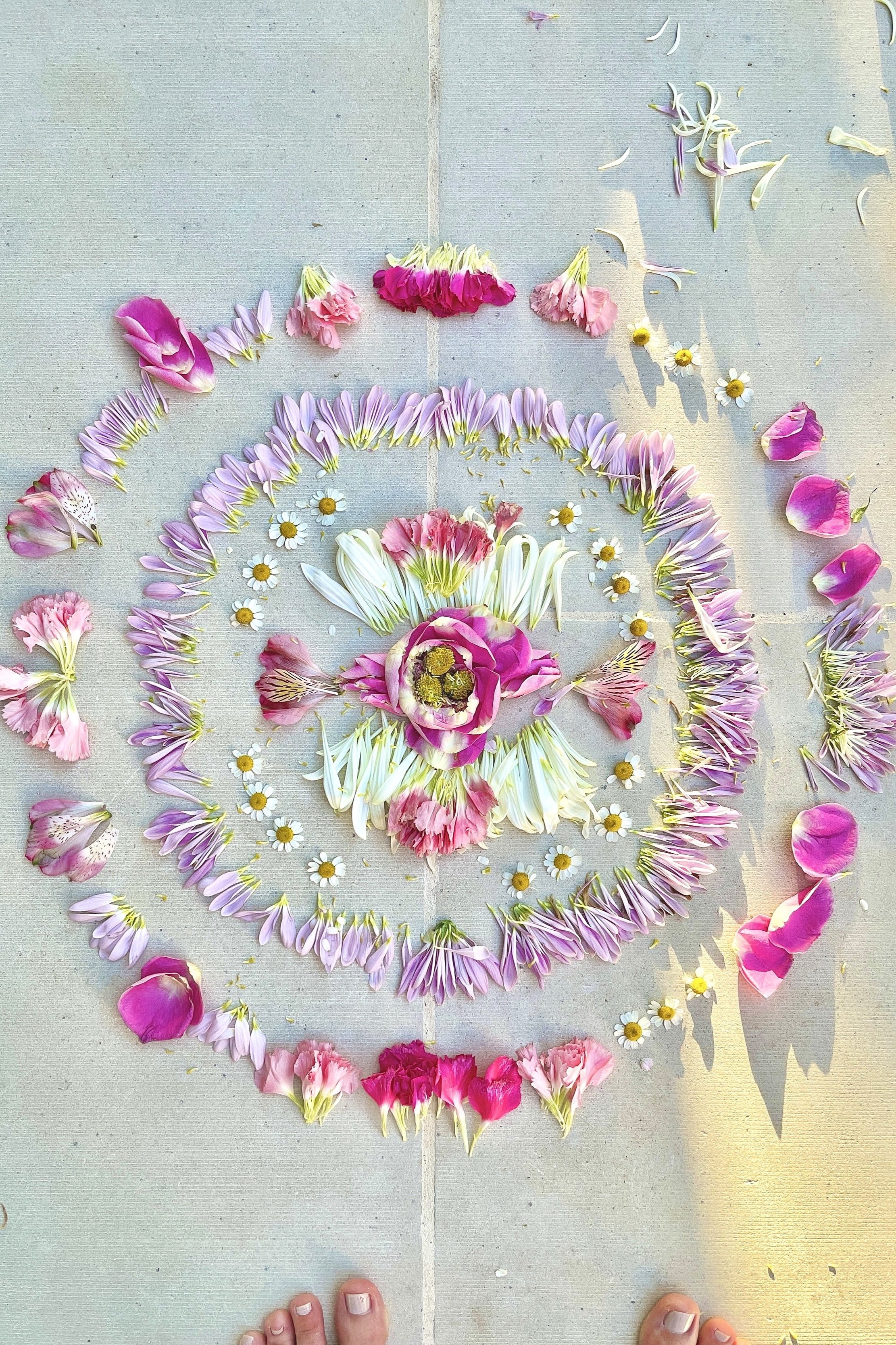 Colorful flowers arranged in a circular spiral pattern on a tiled floor, with some scattered petals nearby.