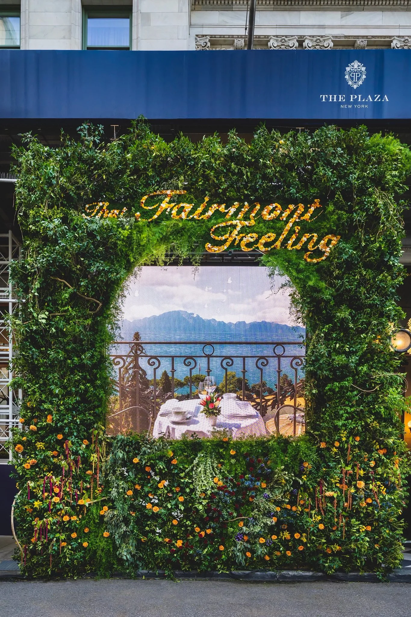 Decorative floral arch with the words 'The Fabulous Feeling' in lights, overlooking a dining table with a mountain view behind a wrought iron railing.