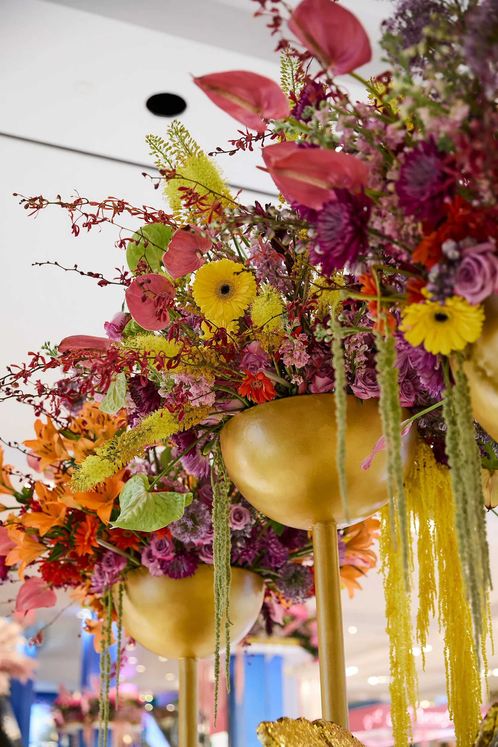 Close-up view of colorful floral arrangements in golden vases on tall stands, featuring pink, yellow, orange, and purple flowers with green foliage.