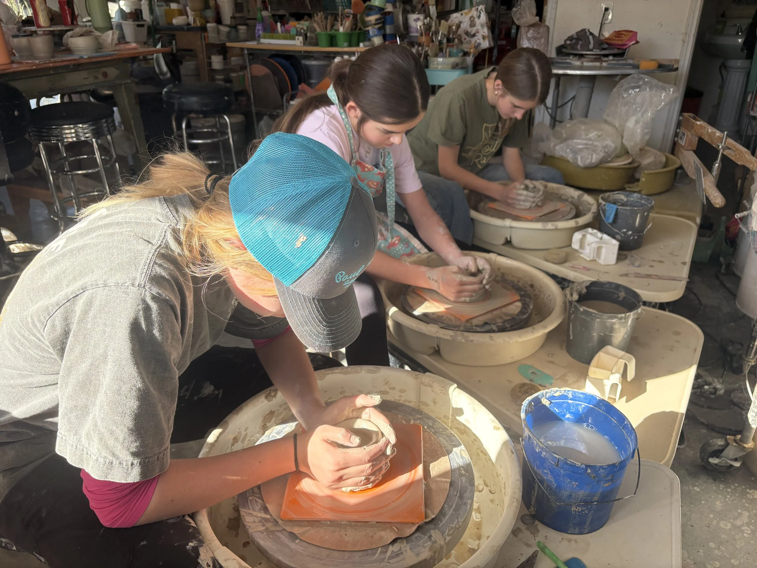 Three students sit a pottery wheels throwing clay in a well equipped pottery studio
