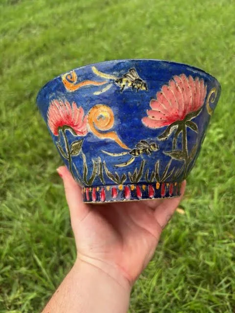 A hand holding a bowl decorated with red flowers and bees on a blue background