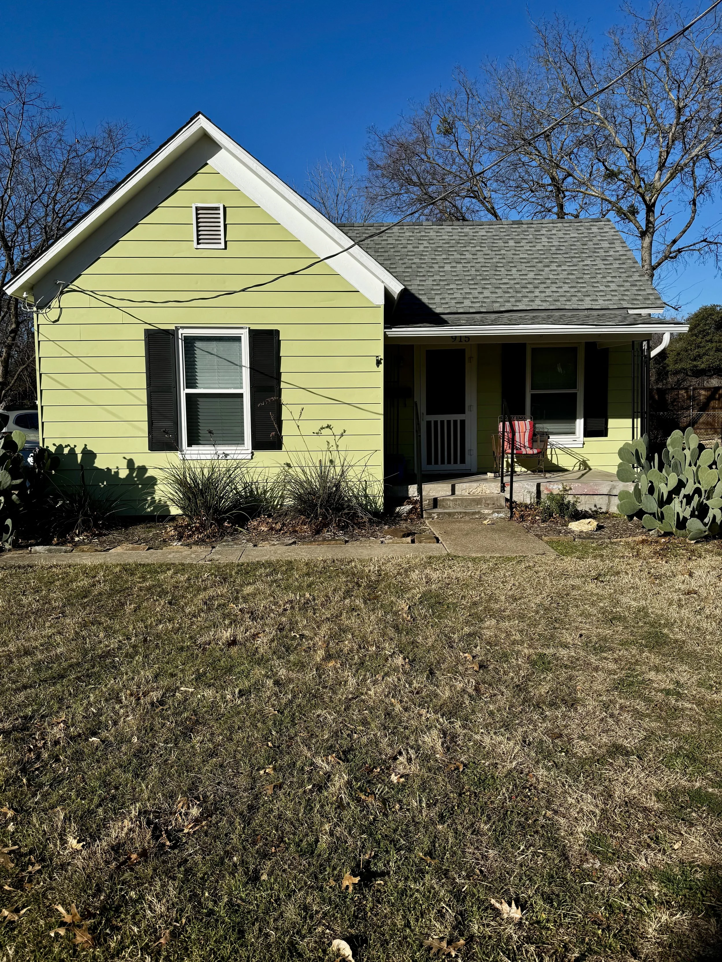 A cute green house with black shutters against a clear blue sky