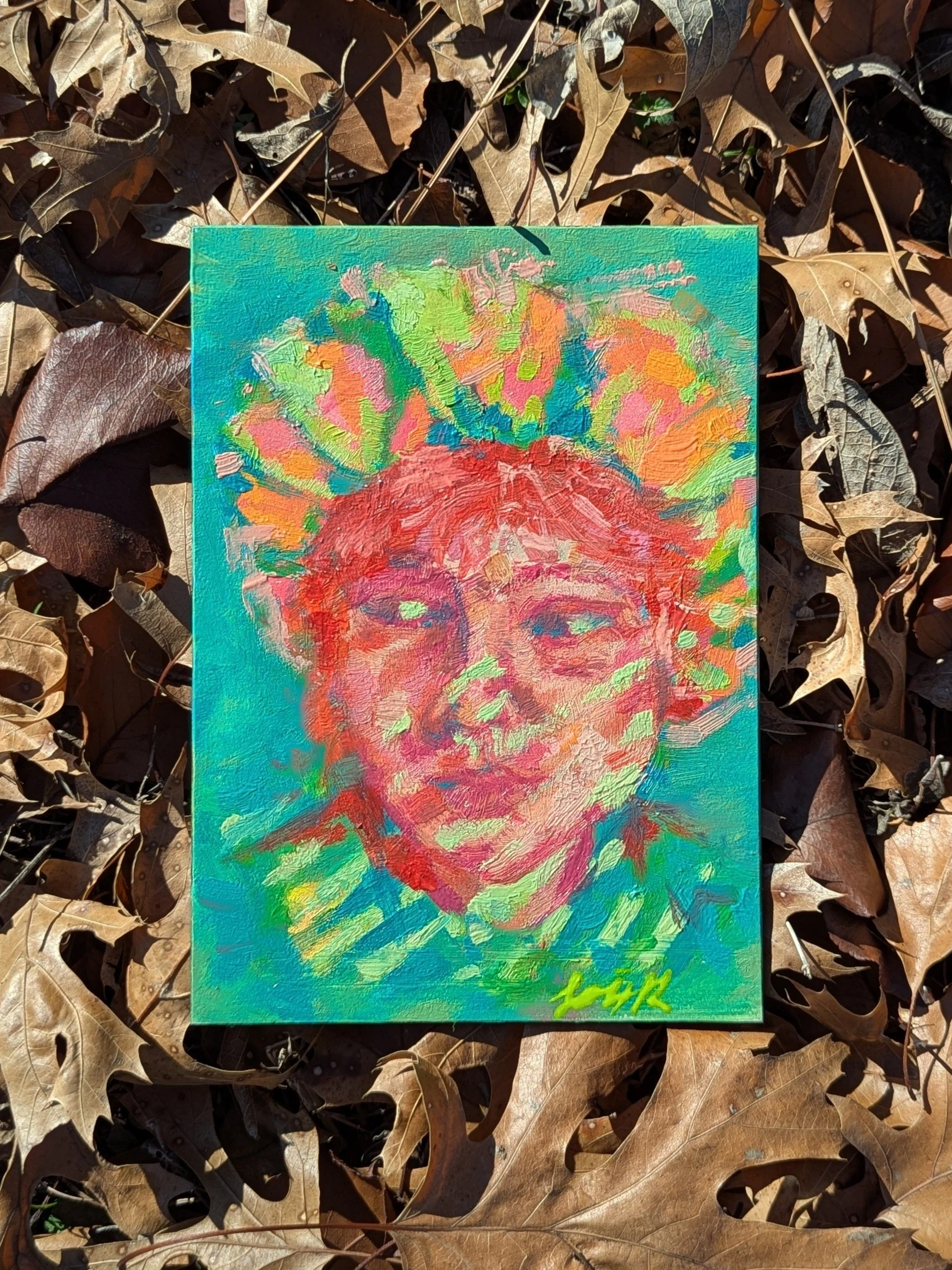 An abstract portrait made with paint and intense warm and cool colors resting in a bed of dried leaves