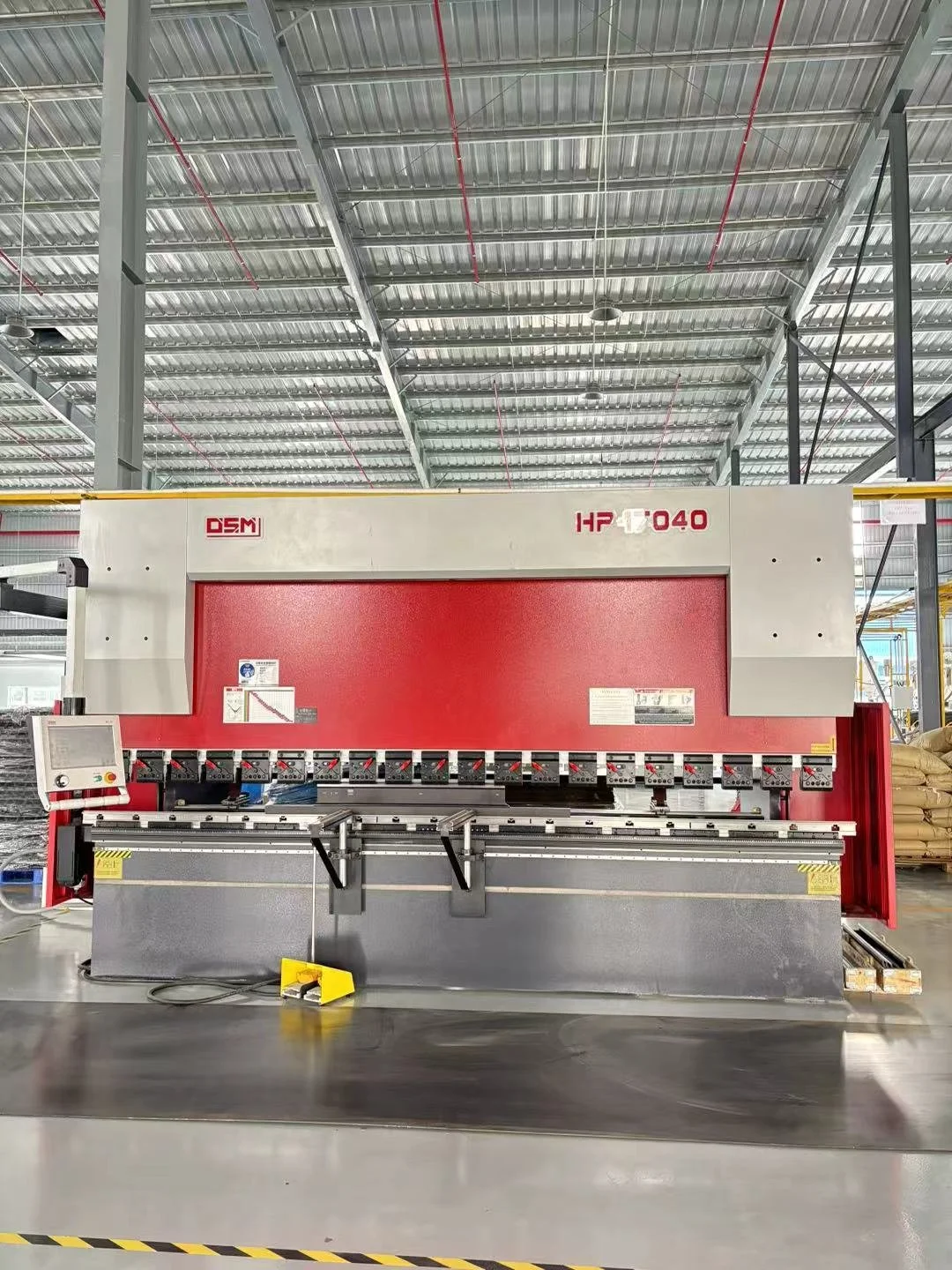 Industrial machine in a warehouse, with a control panel on the left and multiple operating handles, featuring a red and gray color scheme.