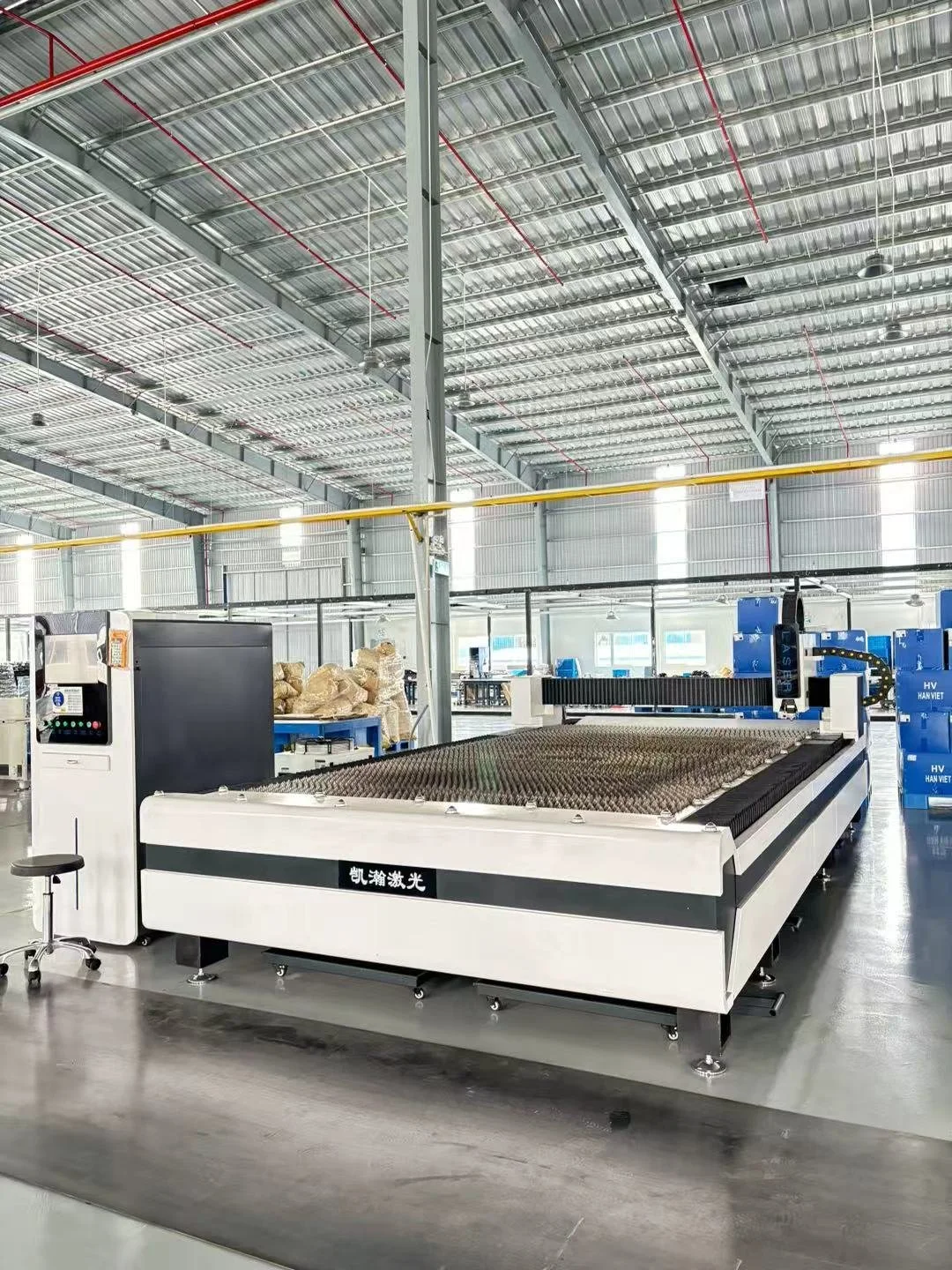 Large industrial laser cutting machine inside a spacious factory with a high metal ceiling, bright lighting, and a smooth concrete floor.