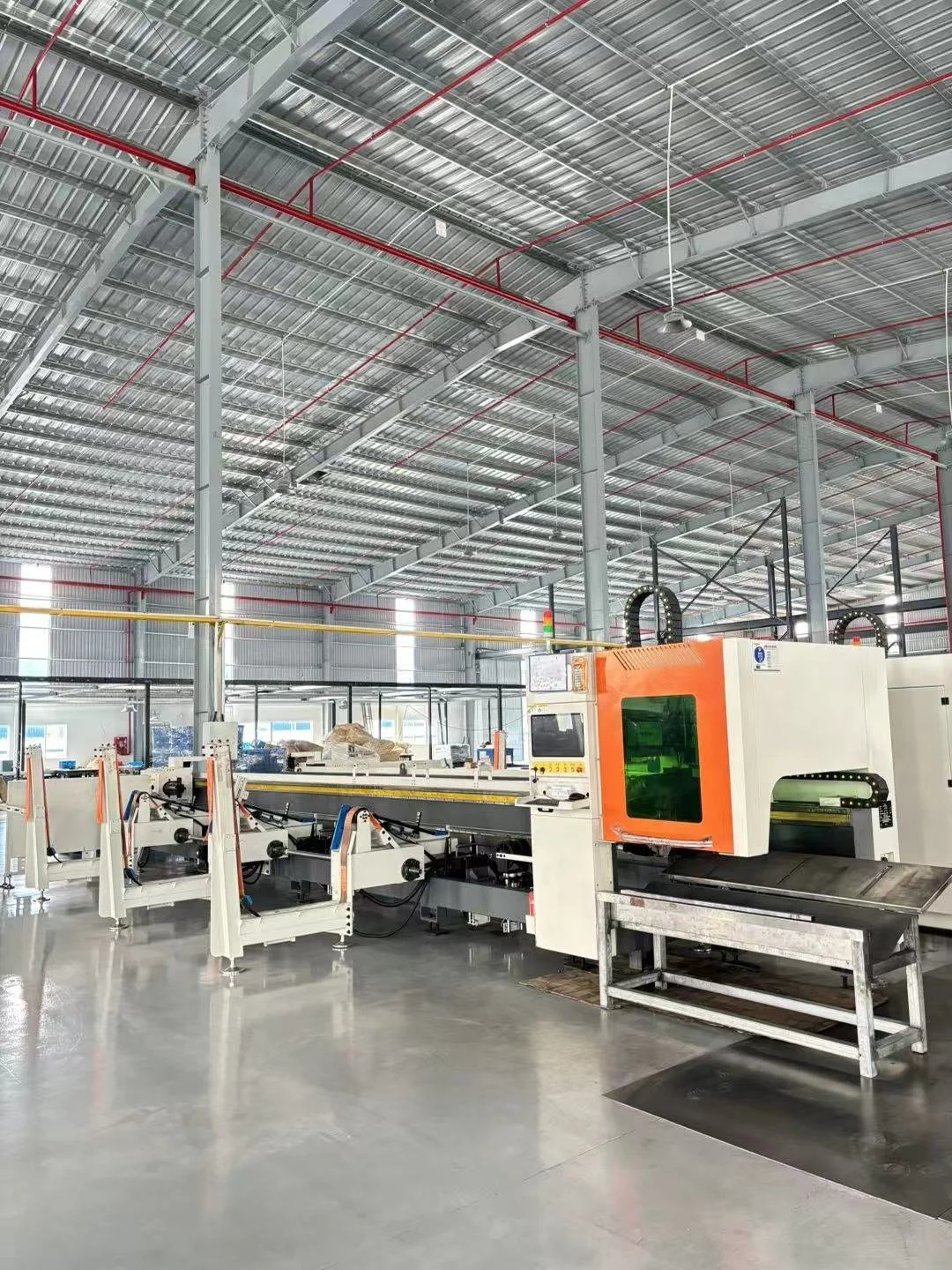 Interior view of a modern industrial manufacturing facility with automated machinery and a high ceiling with metal beams and piping.