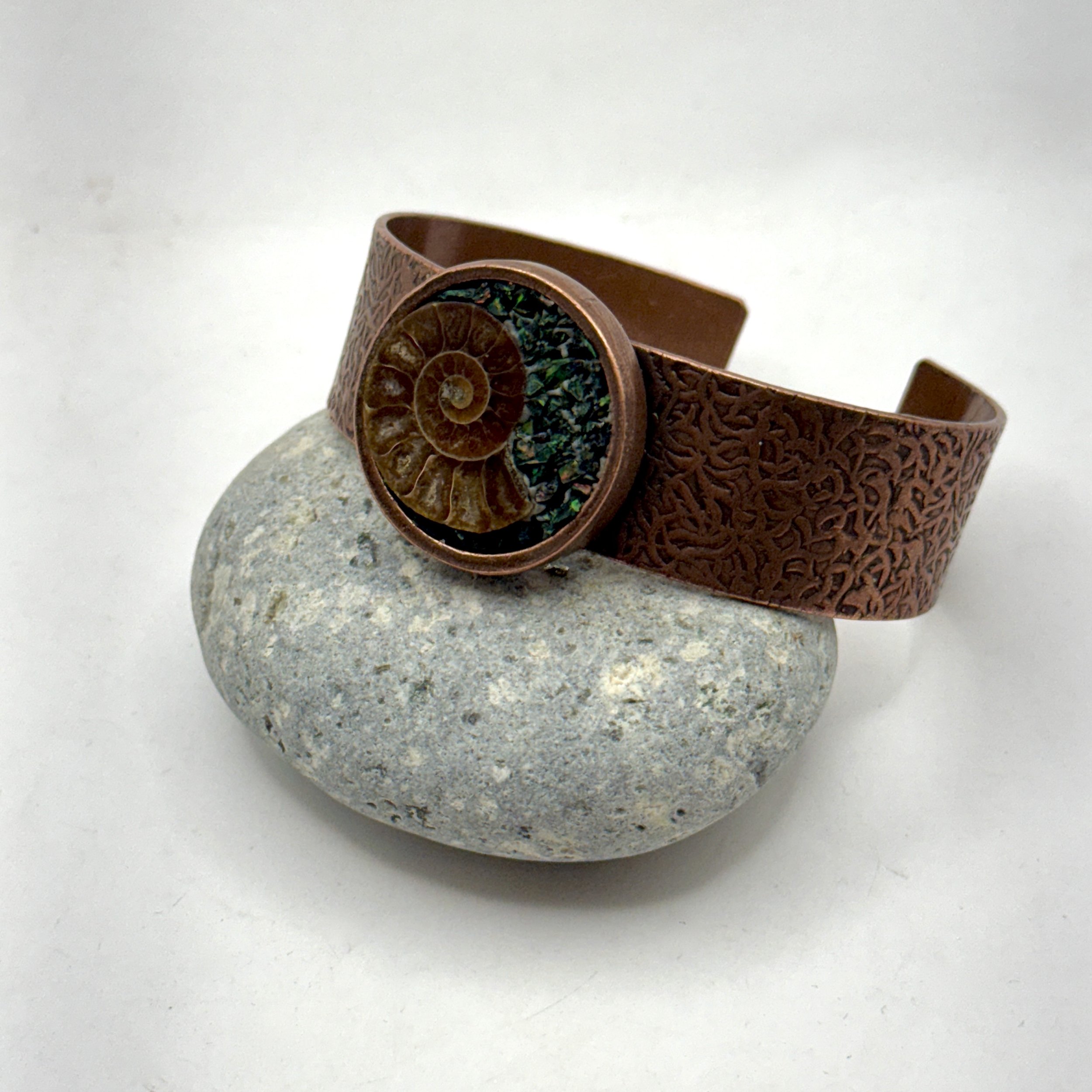 Hammered copper bracelet, 1 1/4” circle on 3/4” wide band. Contains an ammonite fossil and manufactured opal chips.