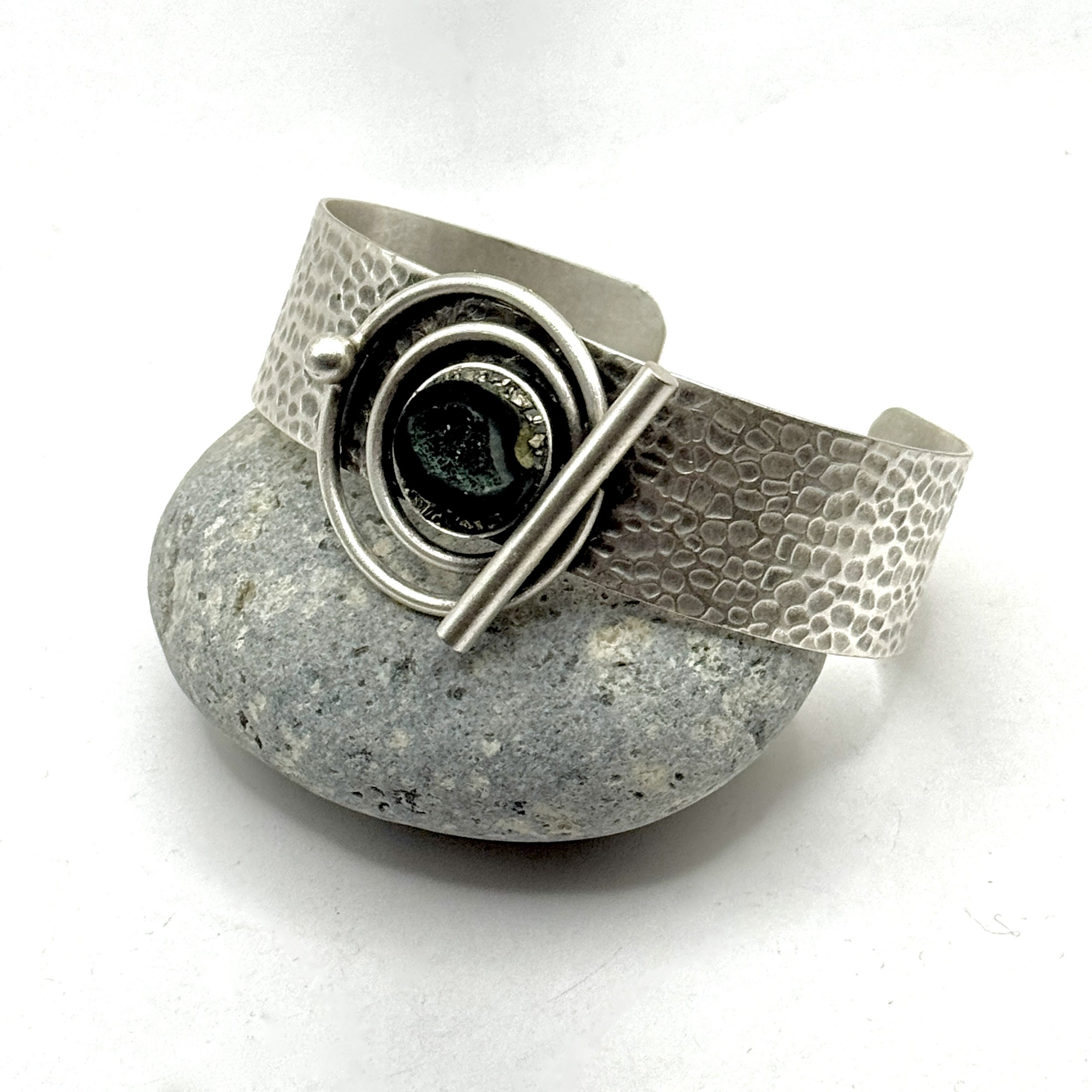 3/4” wide adjustable hammered silver plate band with abstract design holding a geode half and pyrite