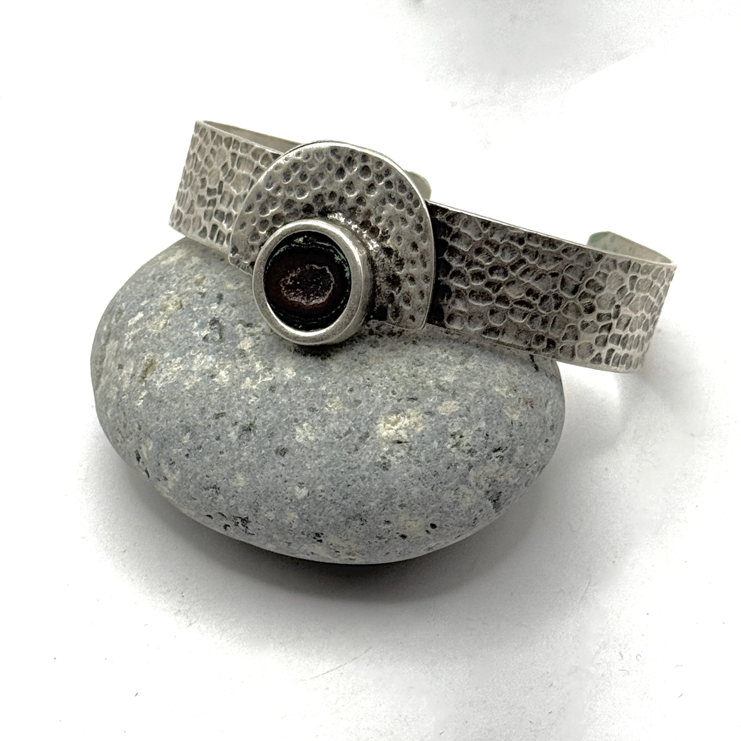 Textured silver plate bracelet with 1/2” wide adjustable band, holding a half geode and pyrite