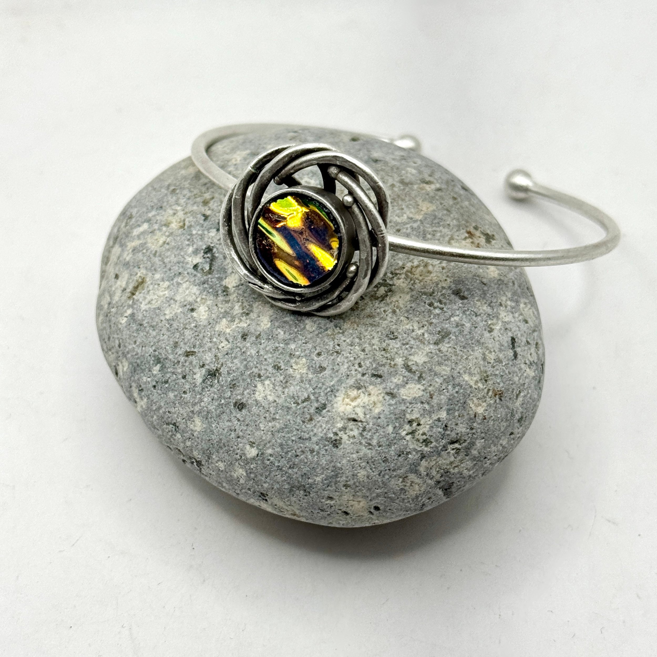 Adjustable bracelet with decorative swirls surrounding a hand cut circle of orange/yellow dichroic glass.