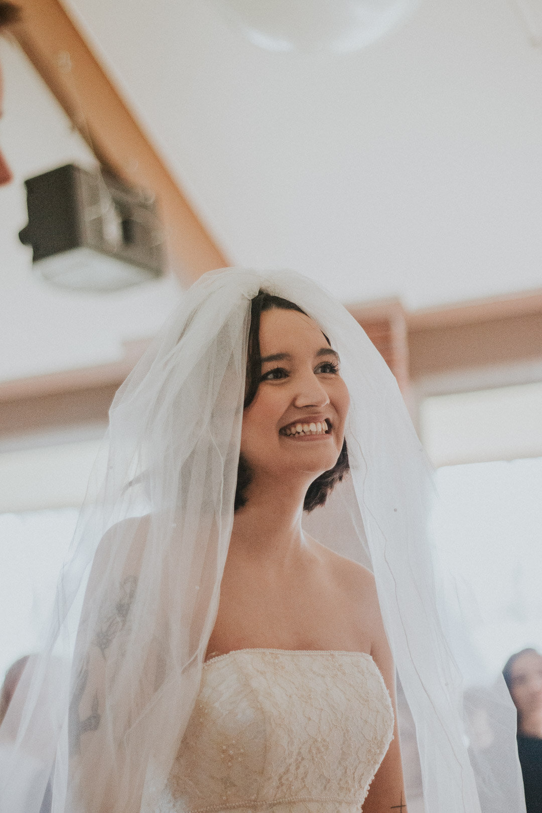 A smiling woman wearing a strapless lace wedding dress with a veil on her head.