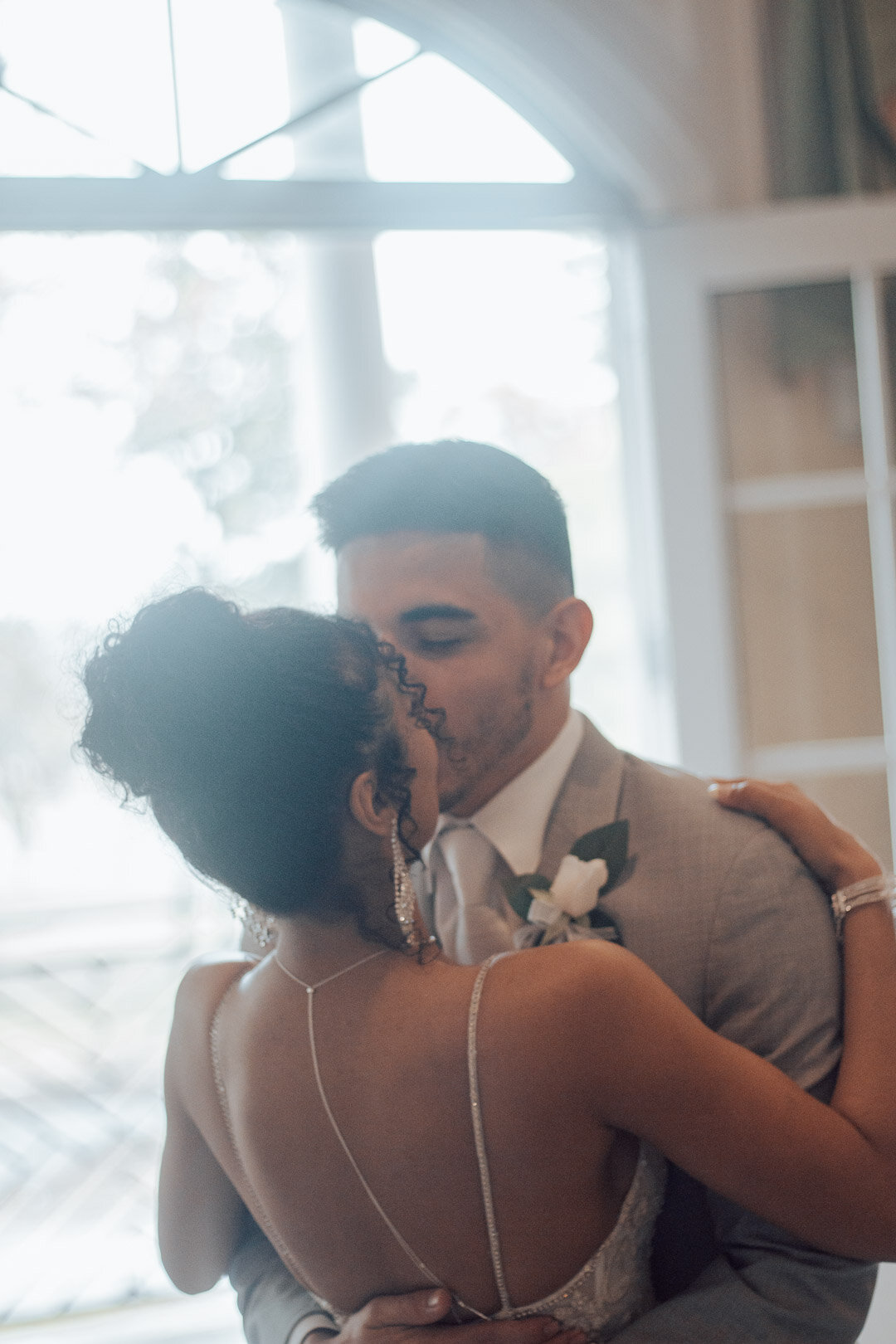 A bride and groom sharing a kiss and dance indoors at their wedding.