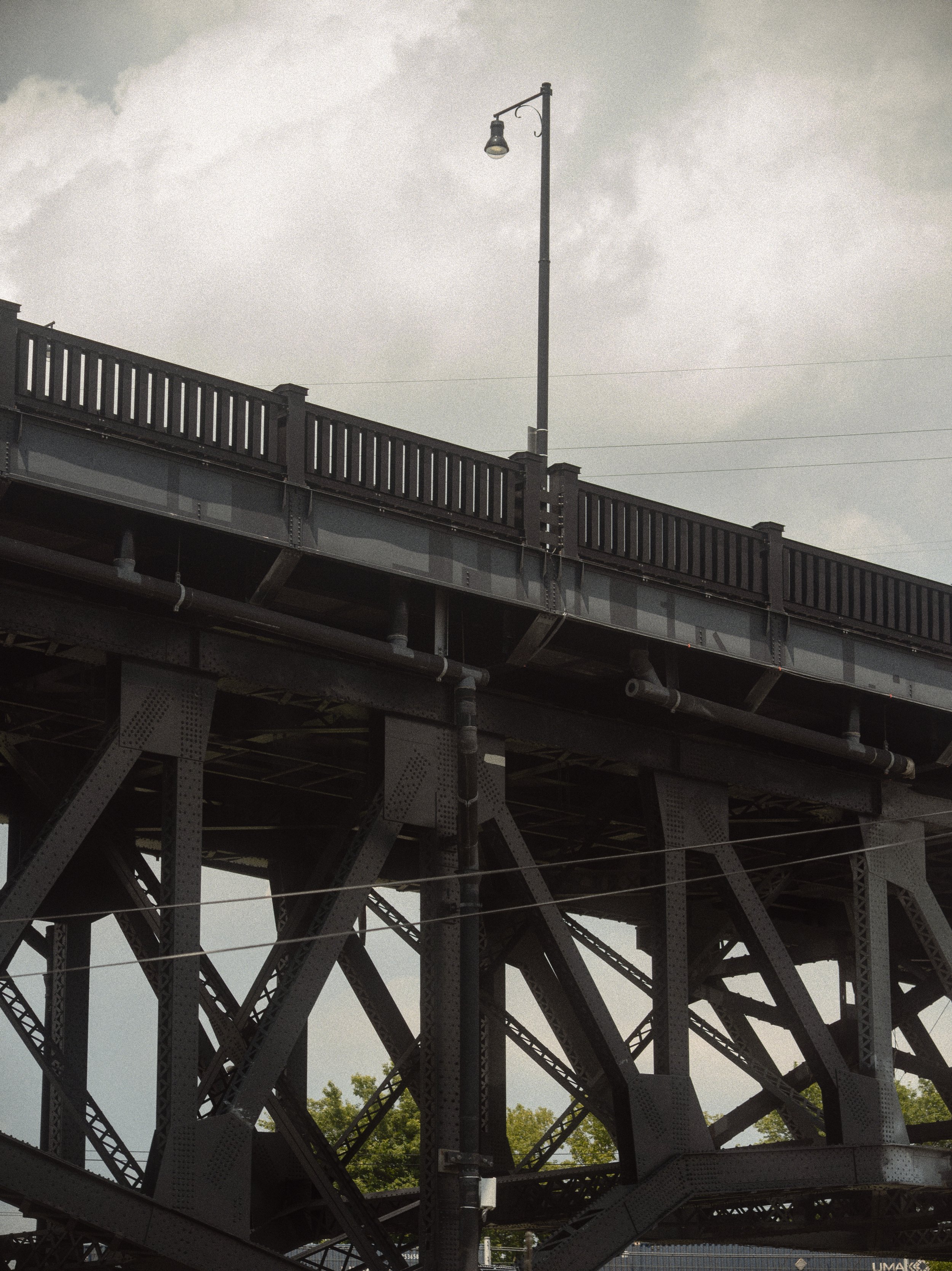 A view of a metal bridge with a railing and a street light pole, under a cloudy sky.