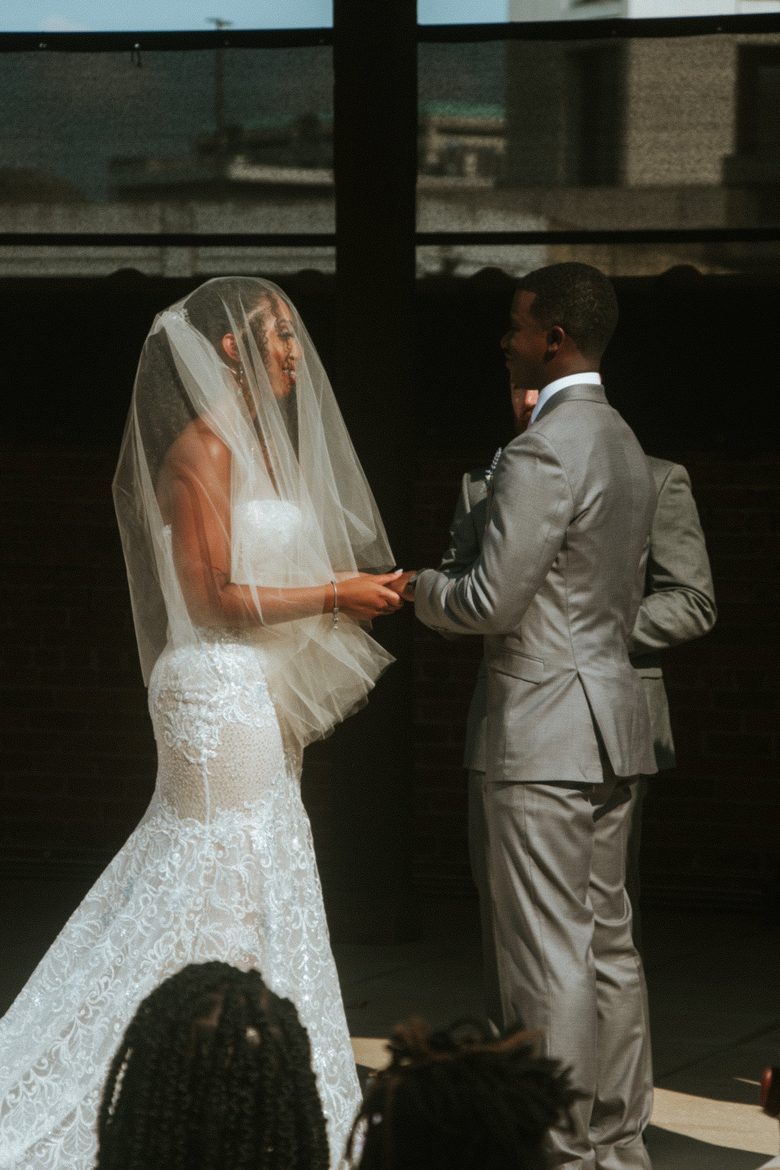 A bride and groom standing face to face during their wedding ceremony, exchanging rings in an indoor setting.