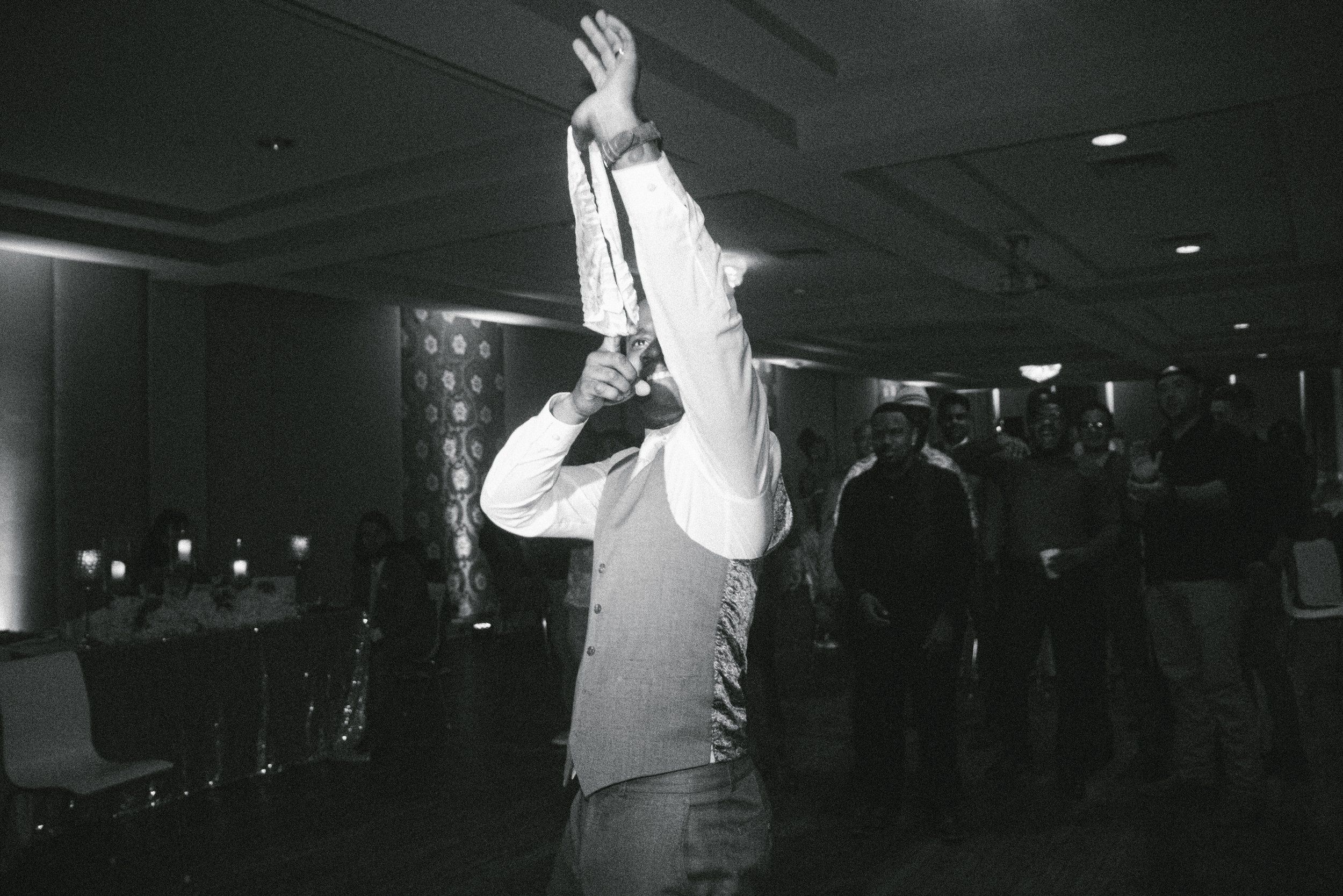 Man in formal attire dancing at an event with onlookers in the background, black and white photo
