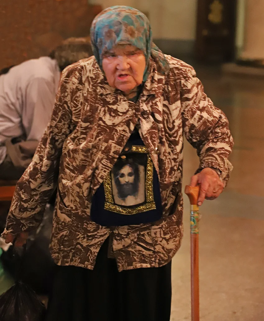 An elderly lady with a large portrait of Christ slung about her neck.