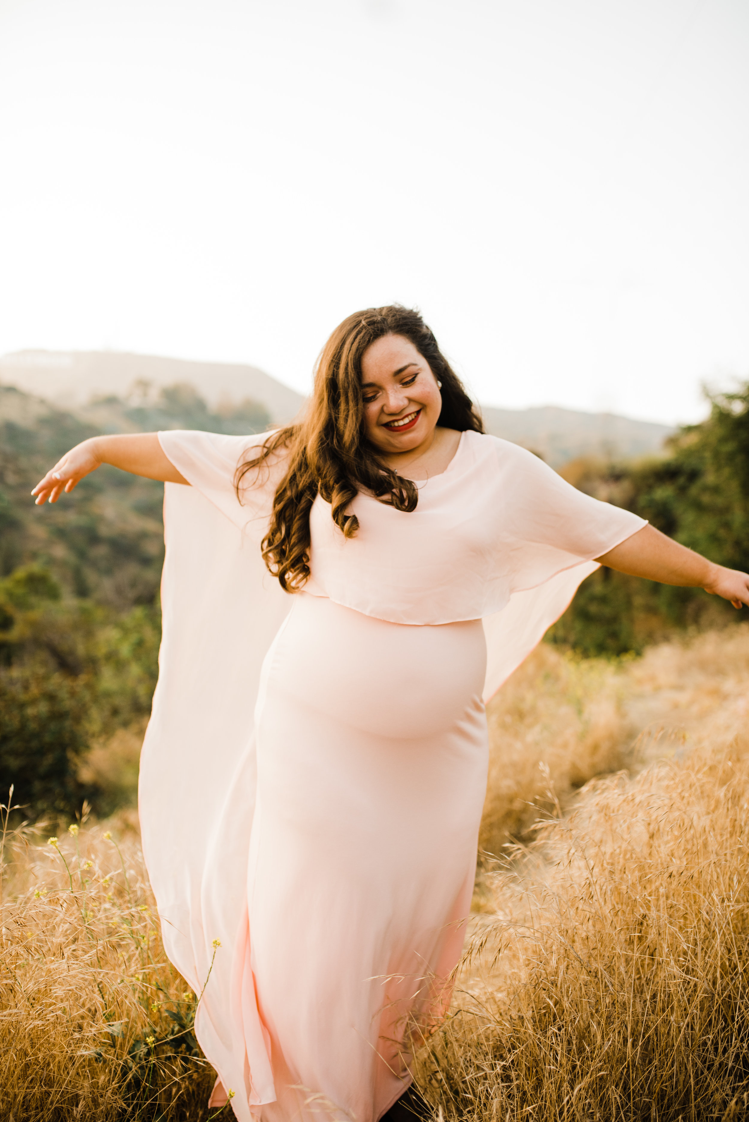 Michelle dancing on the trails in a beautiful pink sheer cape dress for her adventurous engagement session in Los Angeles, California