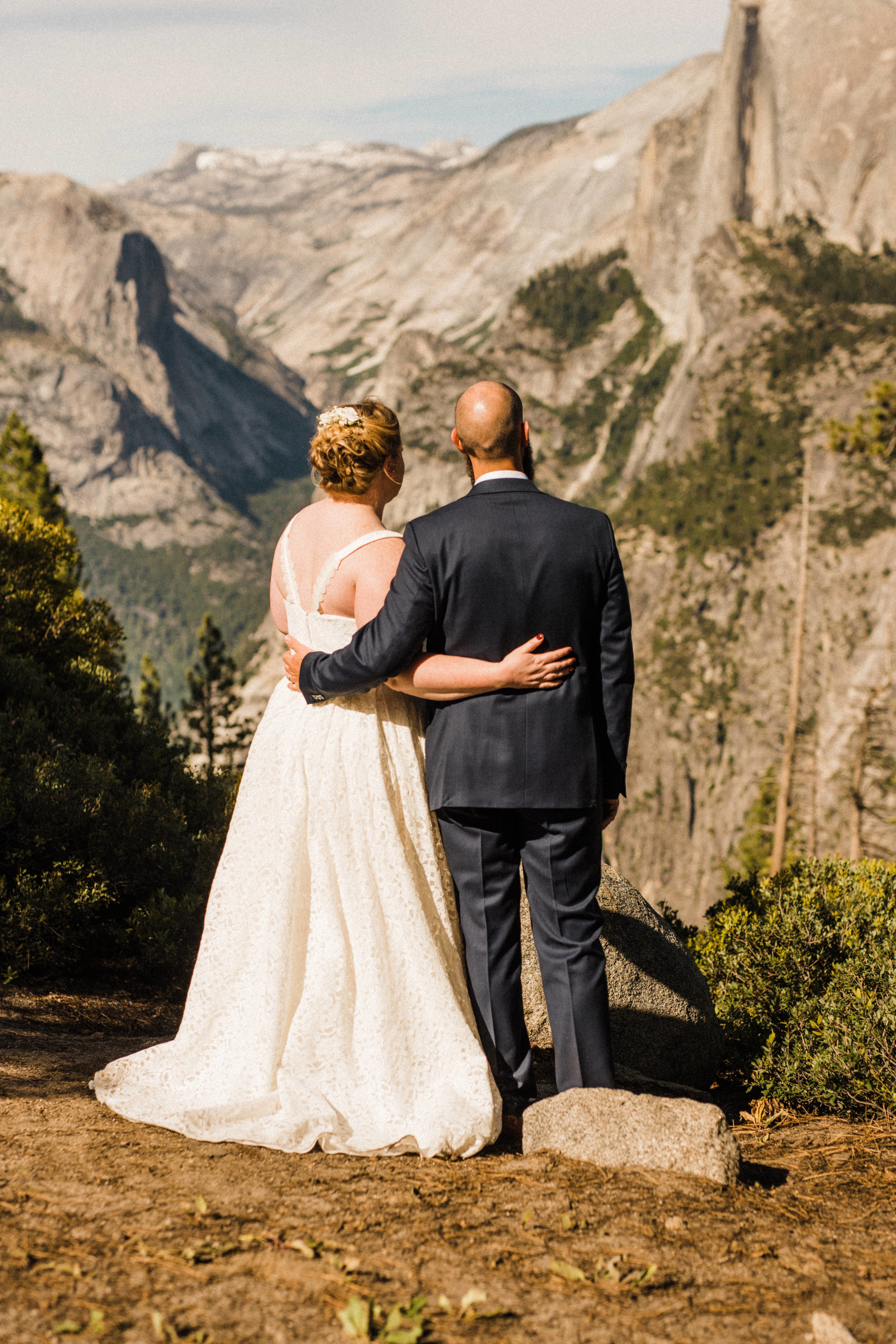 Bride and Groom on the cliff at Glacier Point in Yosemite, facing Half Dome and Yosemite Falls