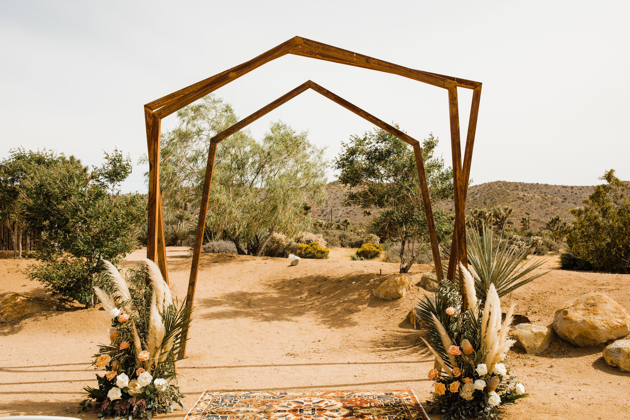 Metal arch at Tumbleweed Sanctuary and Garden Ceremony Site with florals from Pinyon Pine Floral Design. I love the dried pampas grass against the greenery and the pink roses!