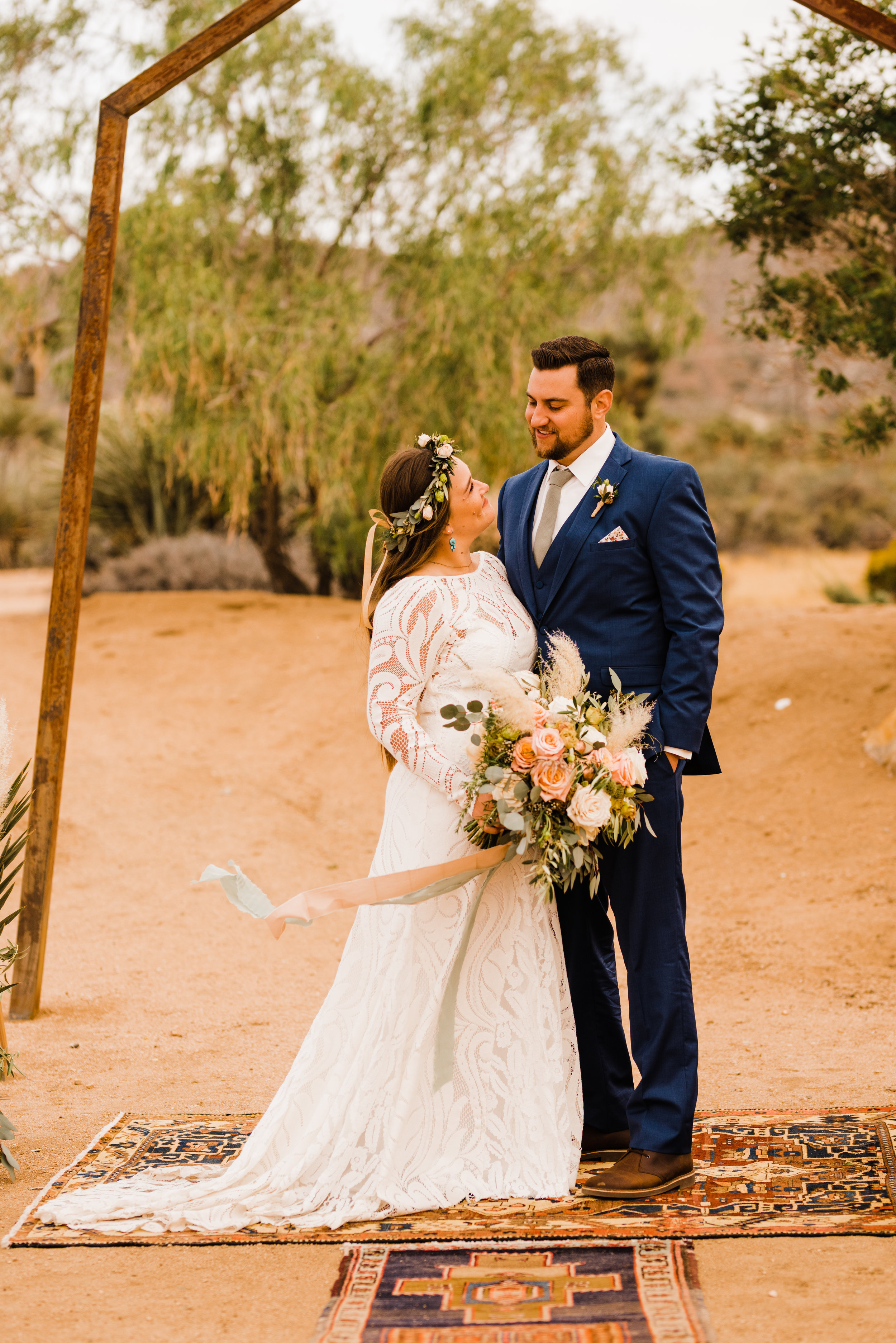 Bride in Lovers Society North Gown with White and Green Flower Crown. Groom in Friar Tux blue suit and pink tie.