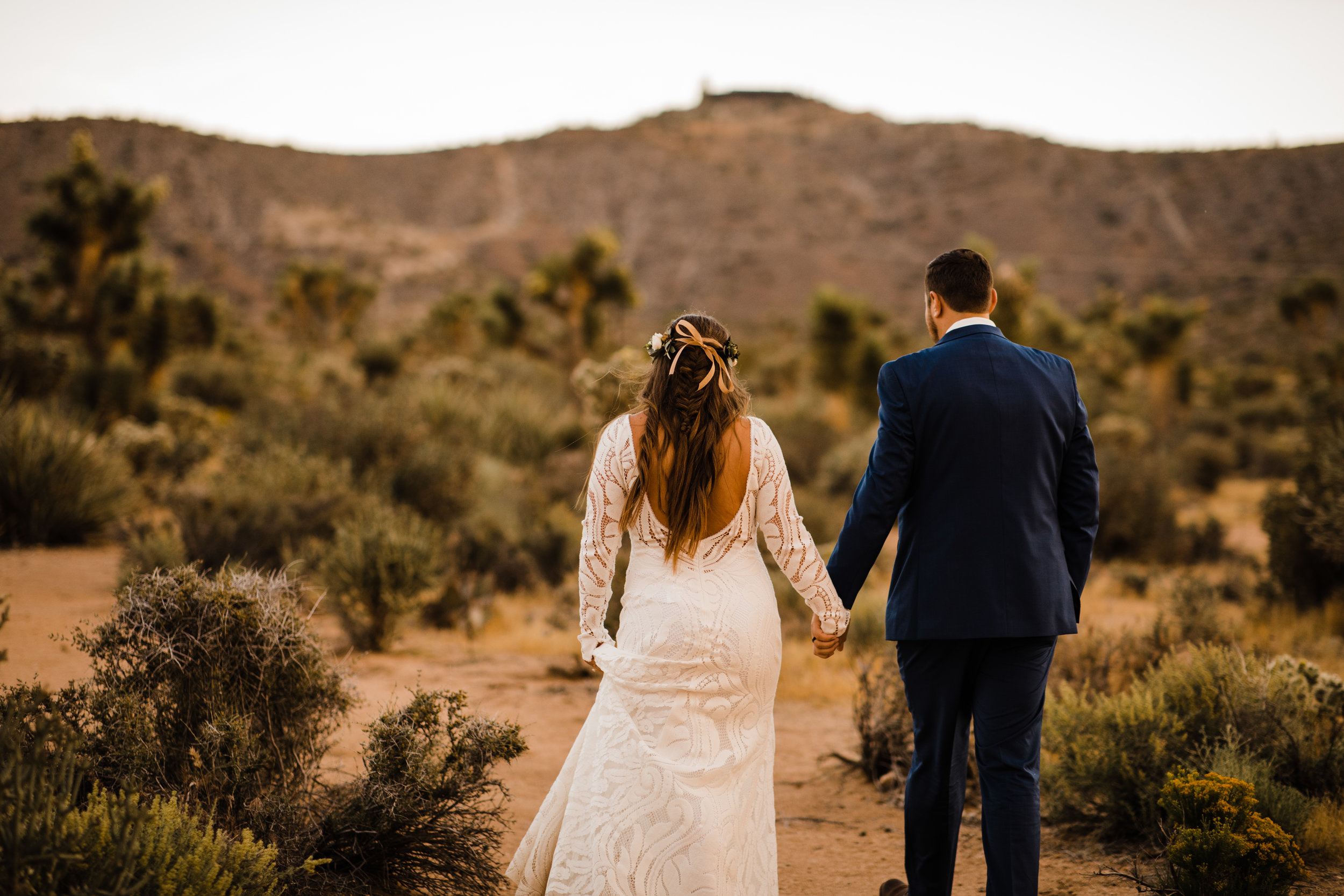 bride and groom walking in joshua tree desert behind tumbleweed wedding venue