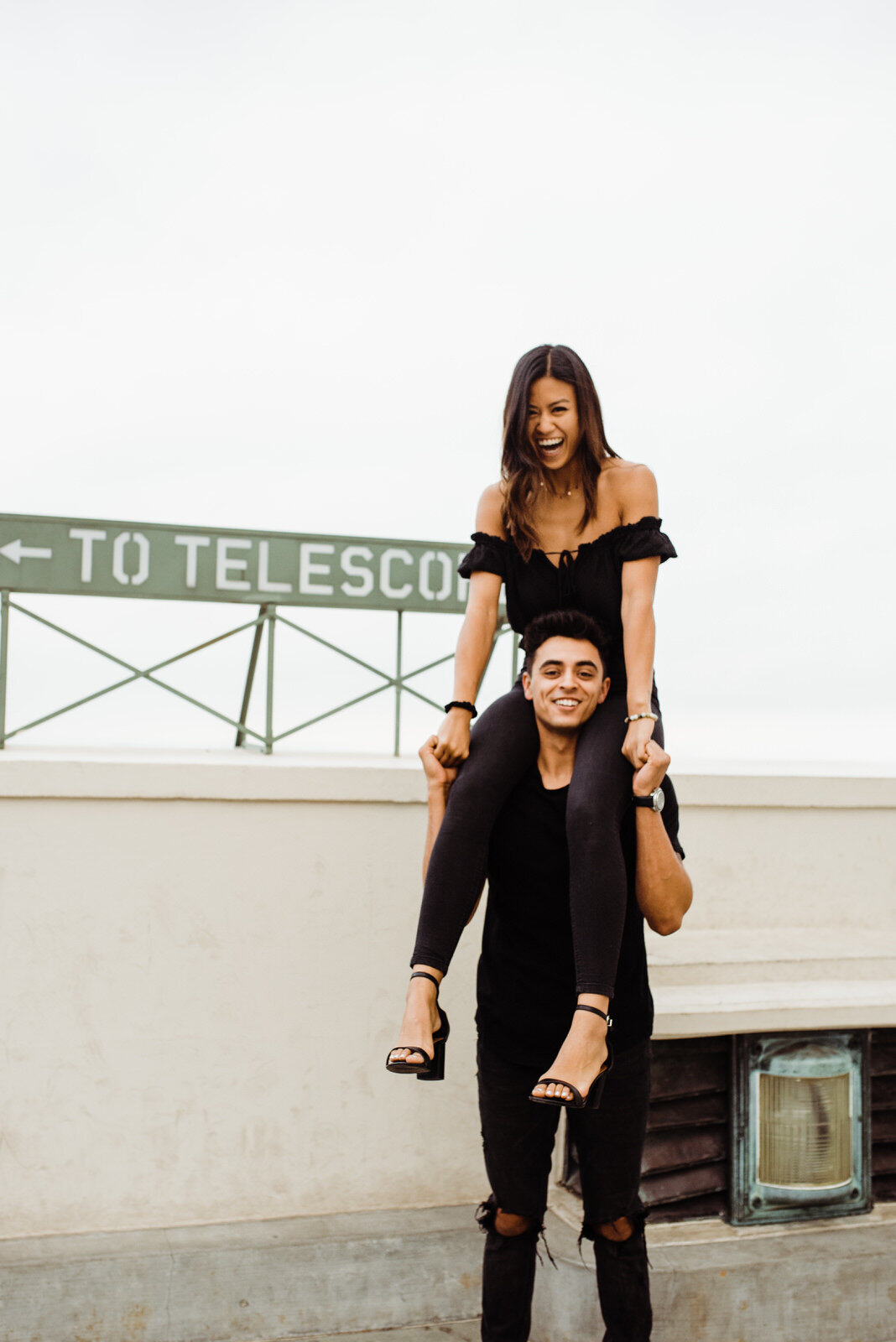 Girl sitting on boy's shoulders during dark and moody engagement session in Griffith Park Los Angeles, Ca