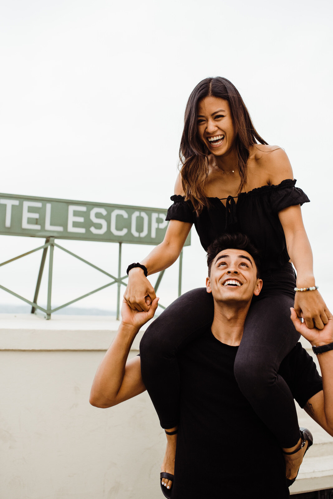 girl laughs on boys shoulders during Griffith Observatory dark and moody engagement session