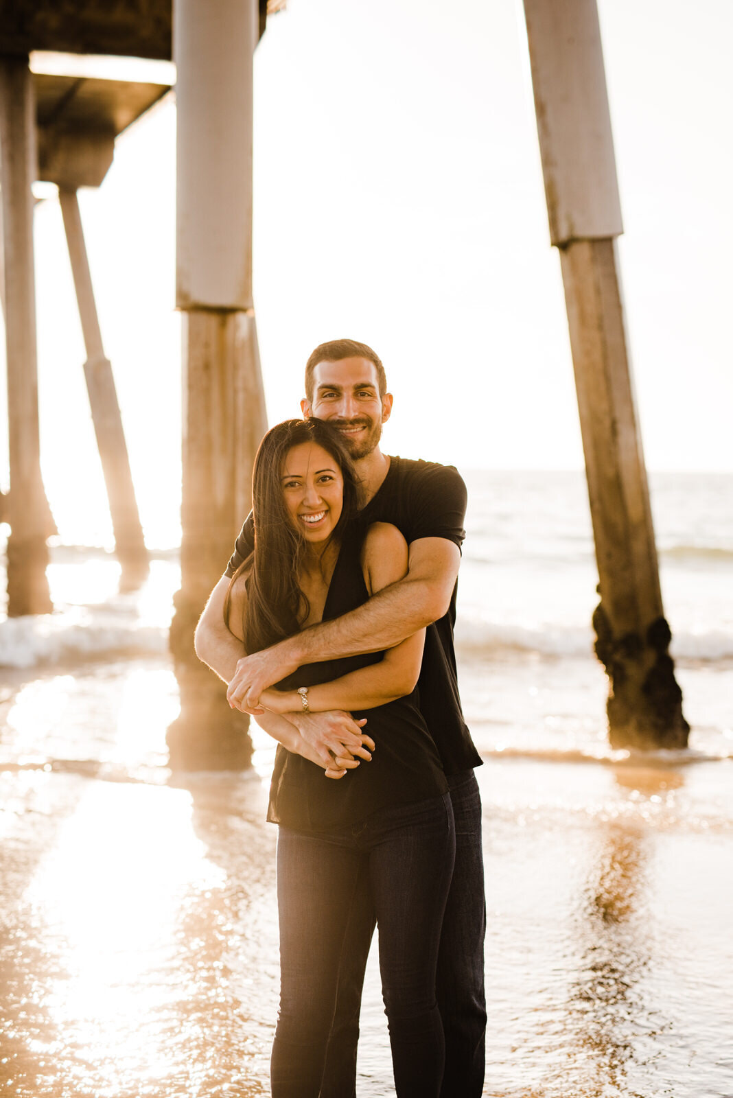 Engaged couple beneath pier at Hermosa Beach