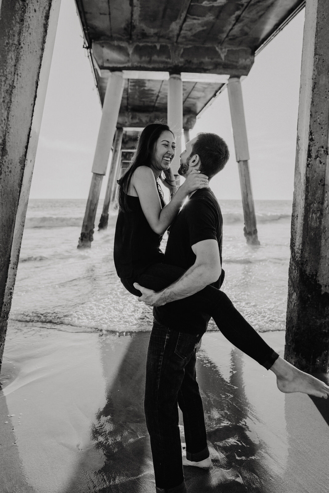 Man holding woman underneath Hermosa Beach Pier